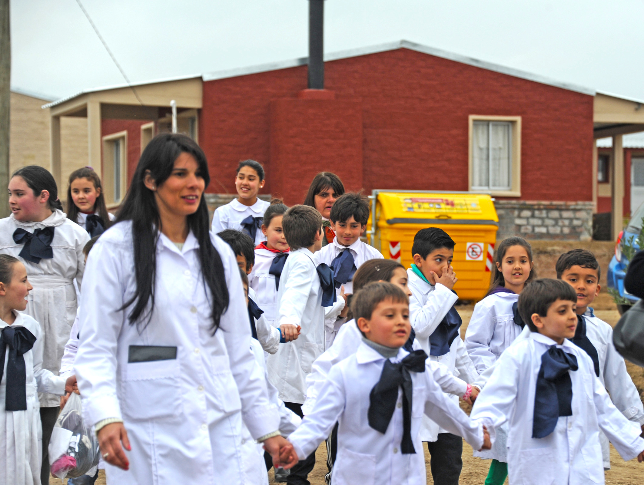 Maestros, y alumnos de la Escuela local, llegan al acto de entrega de viviendas