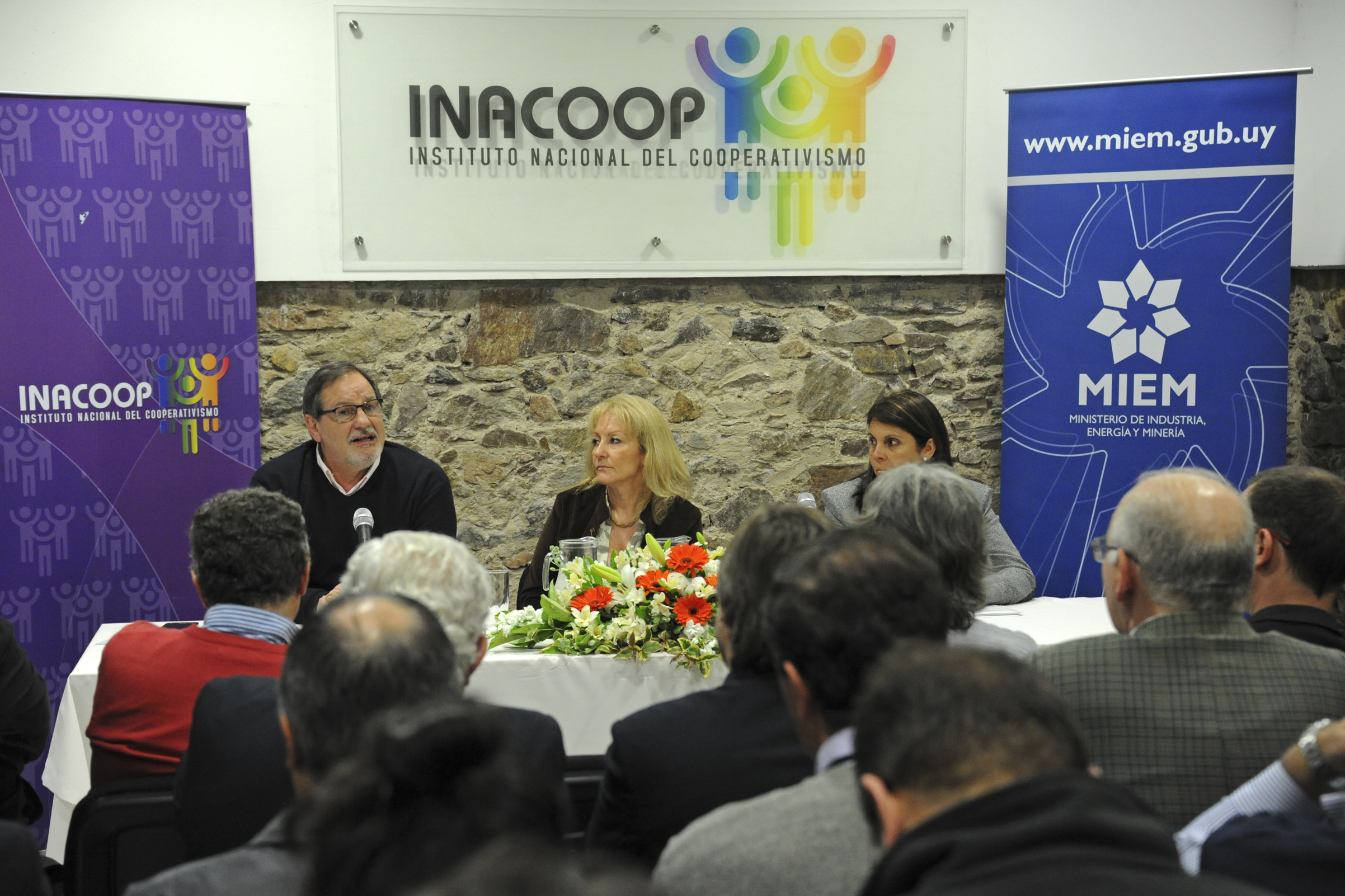Gustavo Bernini, haciendo uso de la palabra, junto a la ministra Carolina Cosse y Rosana Perdomo, presidenta de CUDECOOP