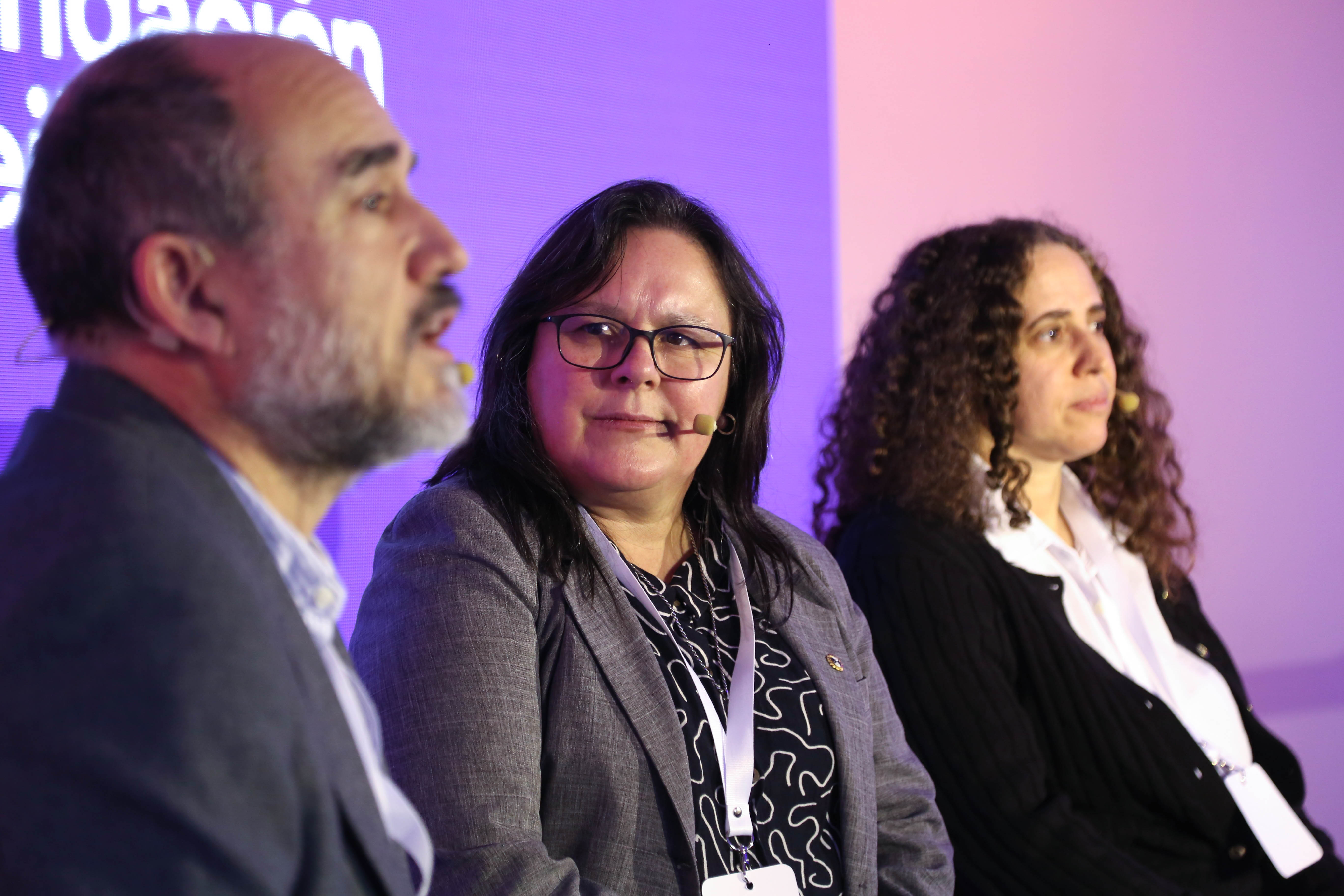 Ministra interina de Educación junto a presidenta de Ceibal y otros disertantes sentados en escenario miran hacia adelante.