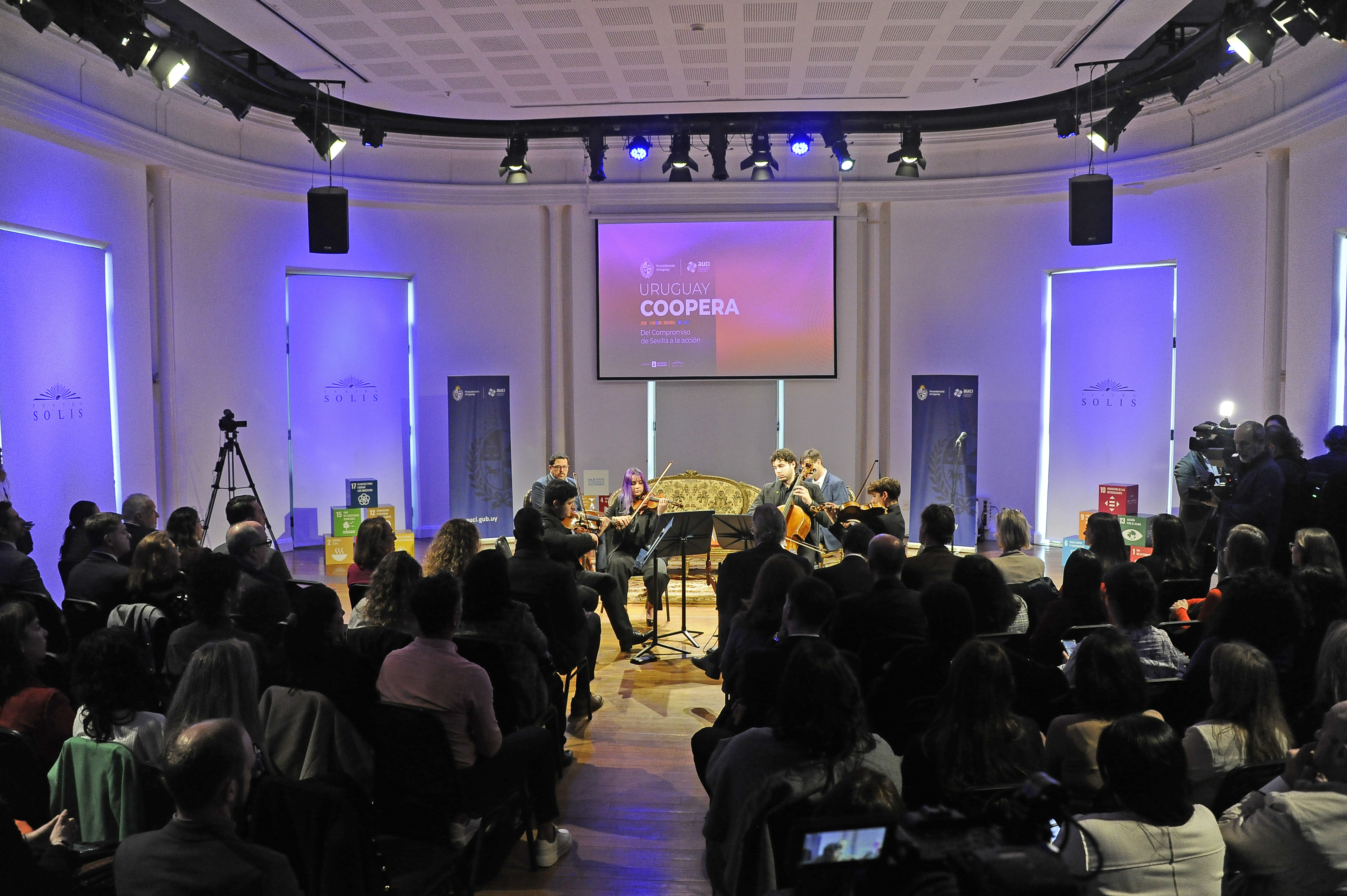 Público, de espaldas, sentado mira a la Orquesta Nacional Juvenil del SODRE tocar en el escenario.