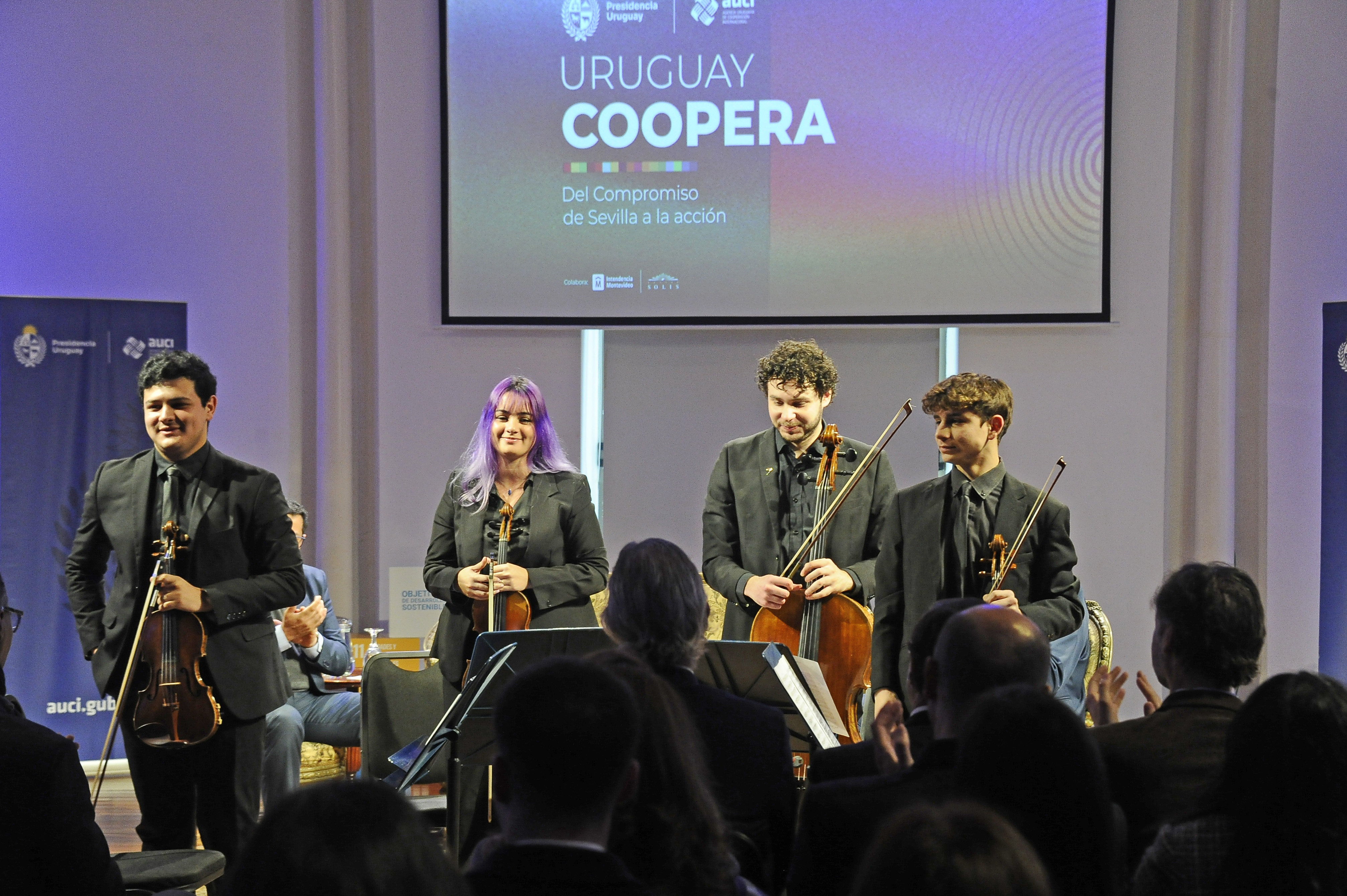 Cuatro integrantes de la Orquesta Nacional Juvenil del SODRE parados en el escenario tras terminar de tocar.