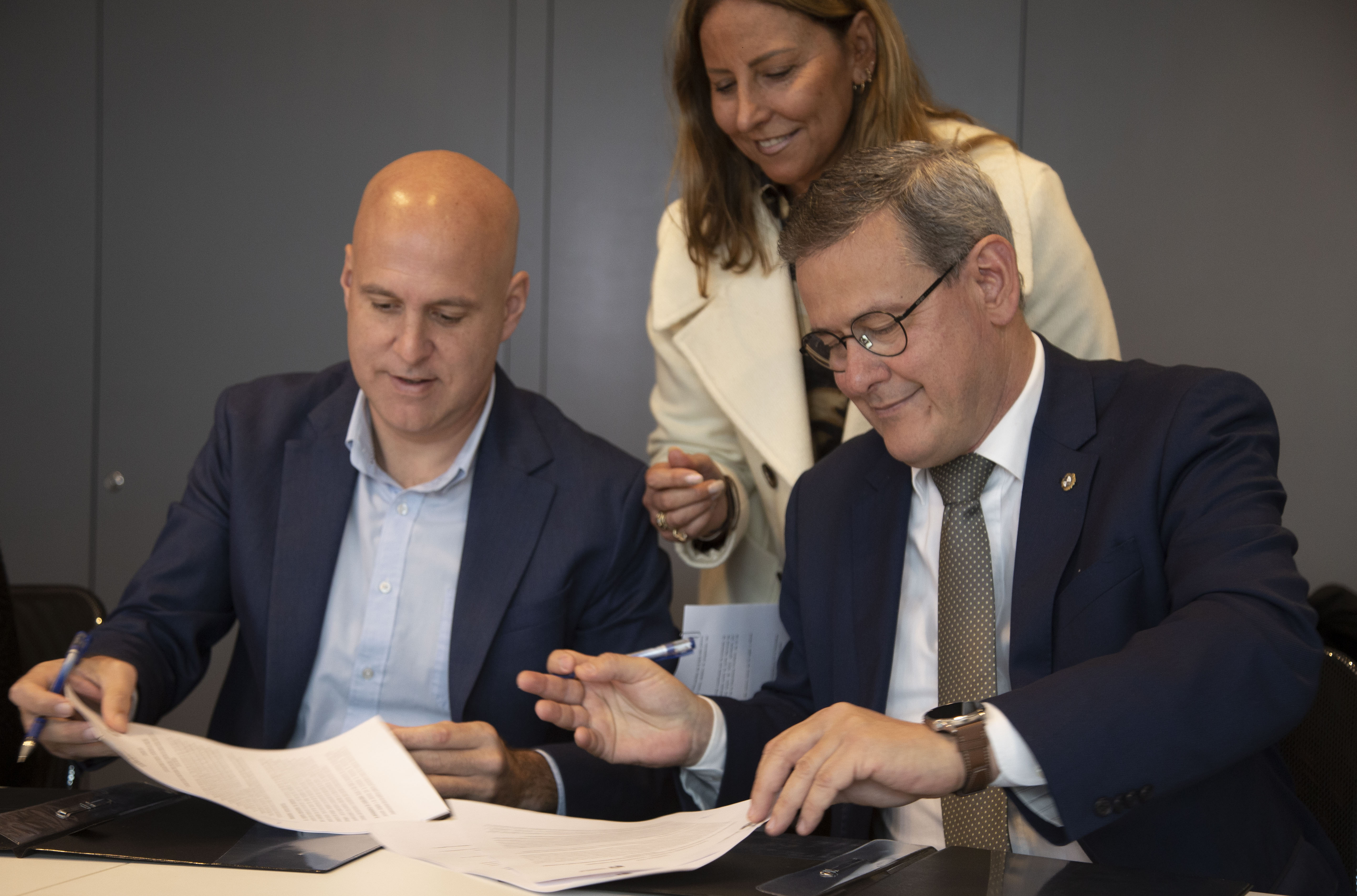 Prosecretario de Presidencia e intendente de Canelones firman documentos sentados en mesa de sala de reuniones. Atrás, una mujer los observa.