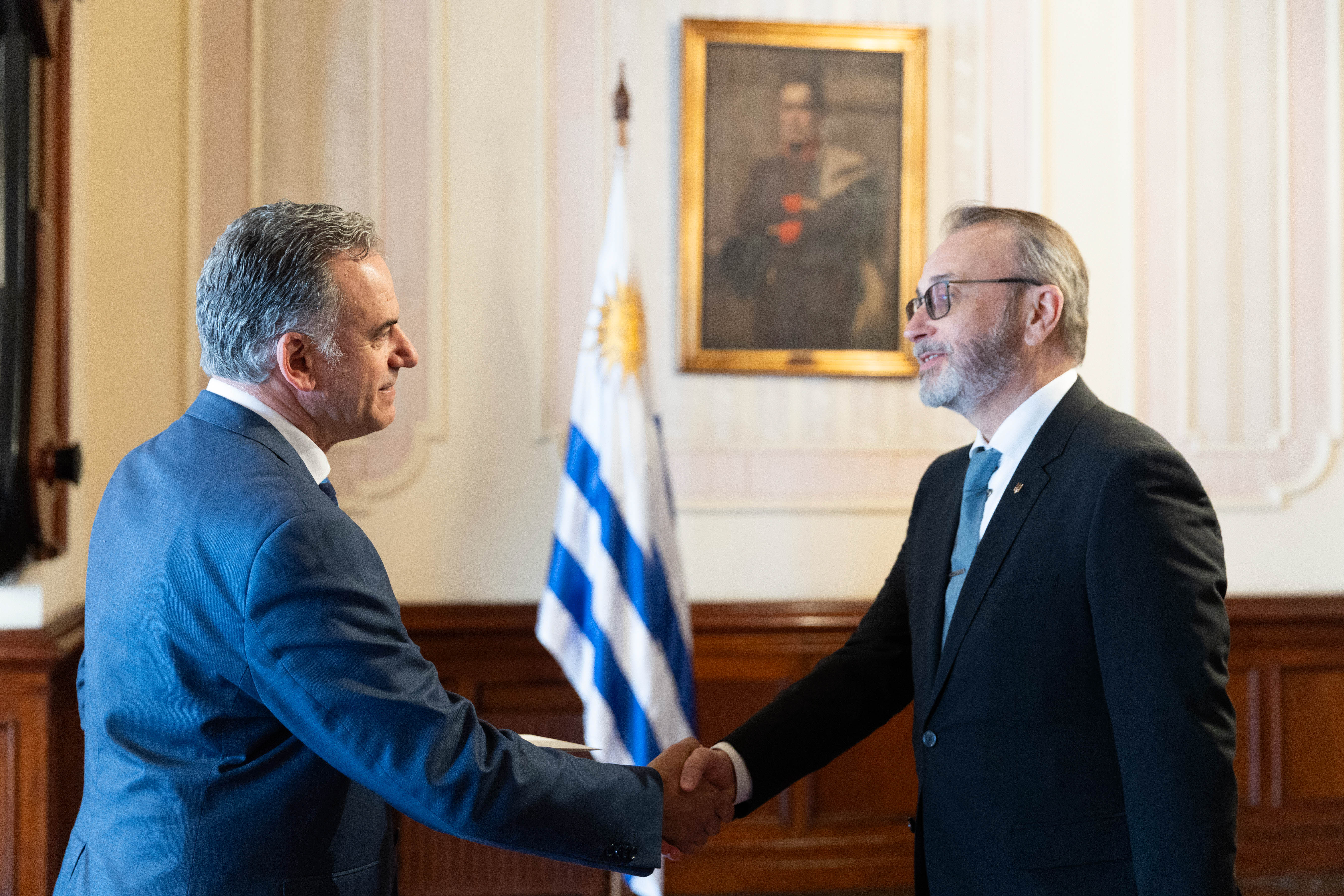 Orsi y el embajador de Ucrania se saludan con la mano en el salón principal del Palacio. Atrás se observa el pabellón nacional