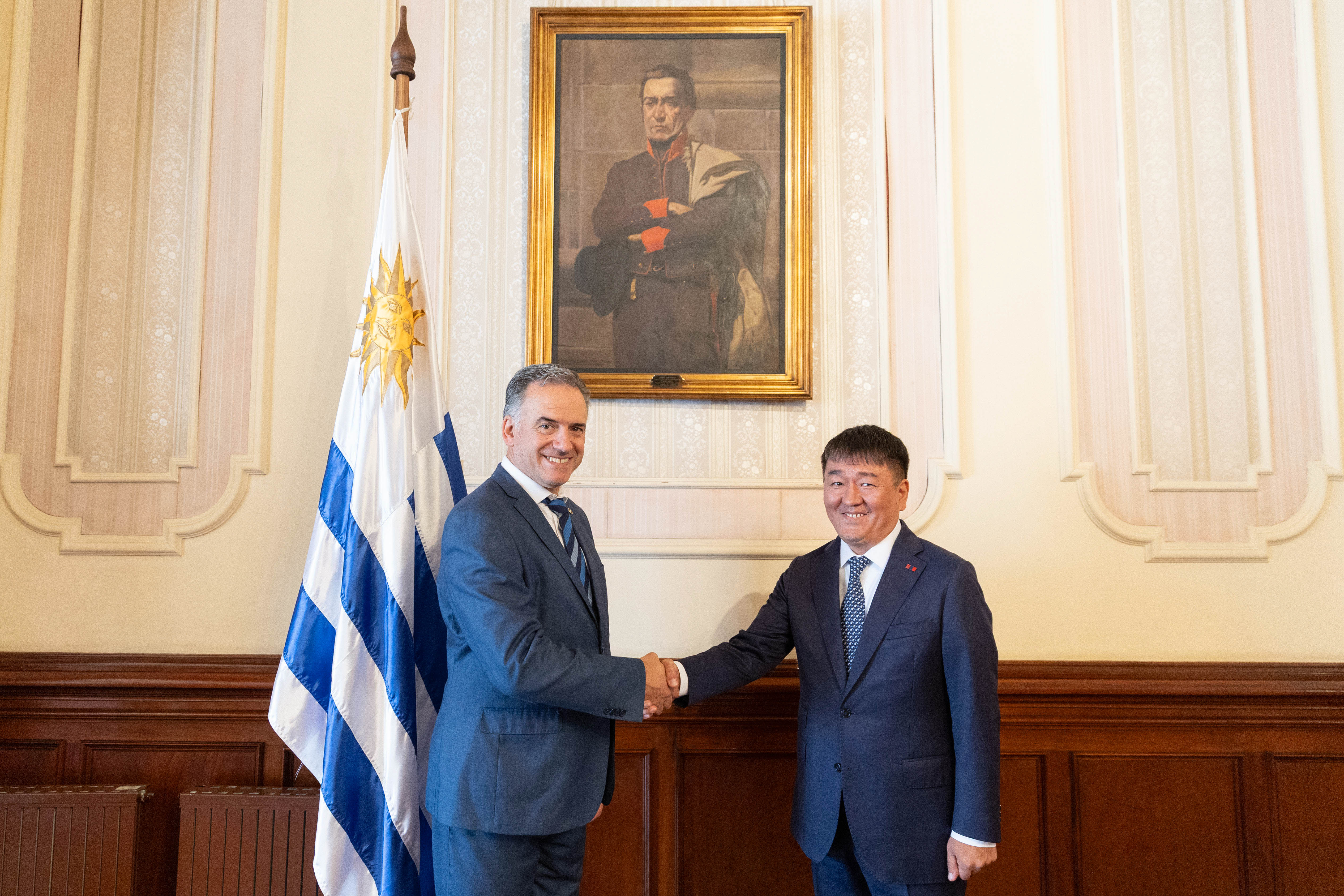 Orsi y embajador de Mongolia posan sonrientes frente a cámara mientras se estrechan las manos.