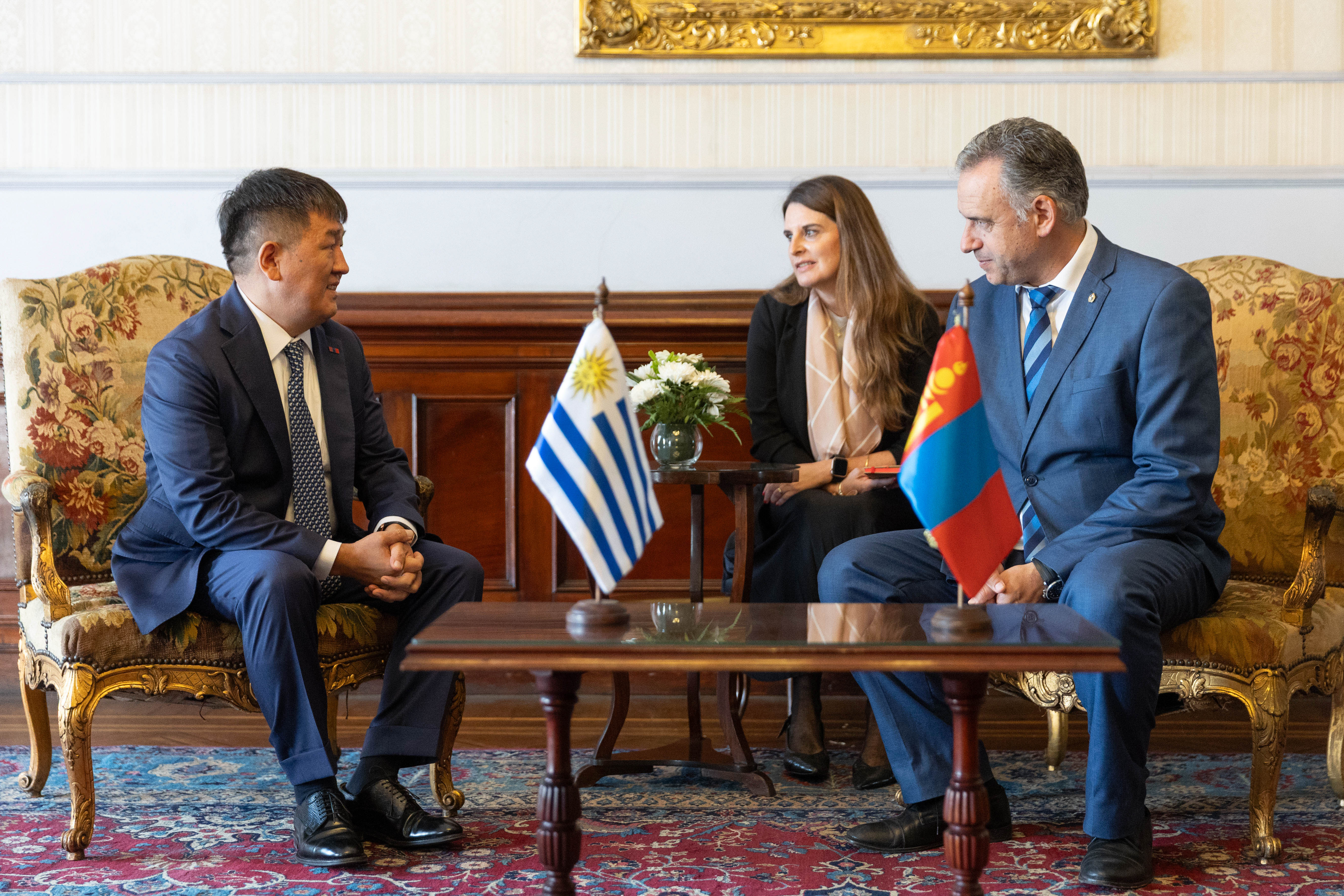 Otra perspectiva de Orsi y embajador de Mongolia sentados en sillones dialogando mientras la traductora los observa.