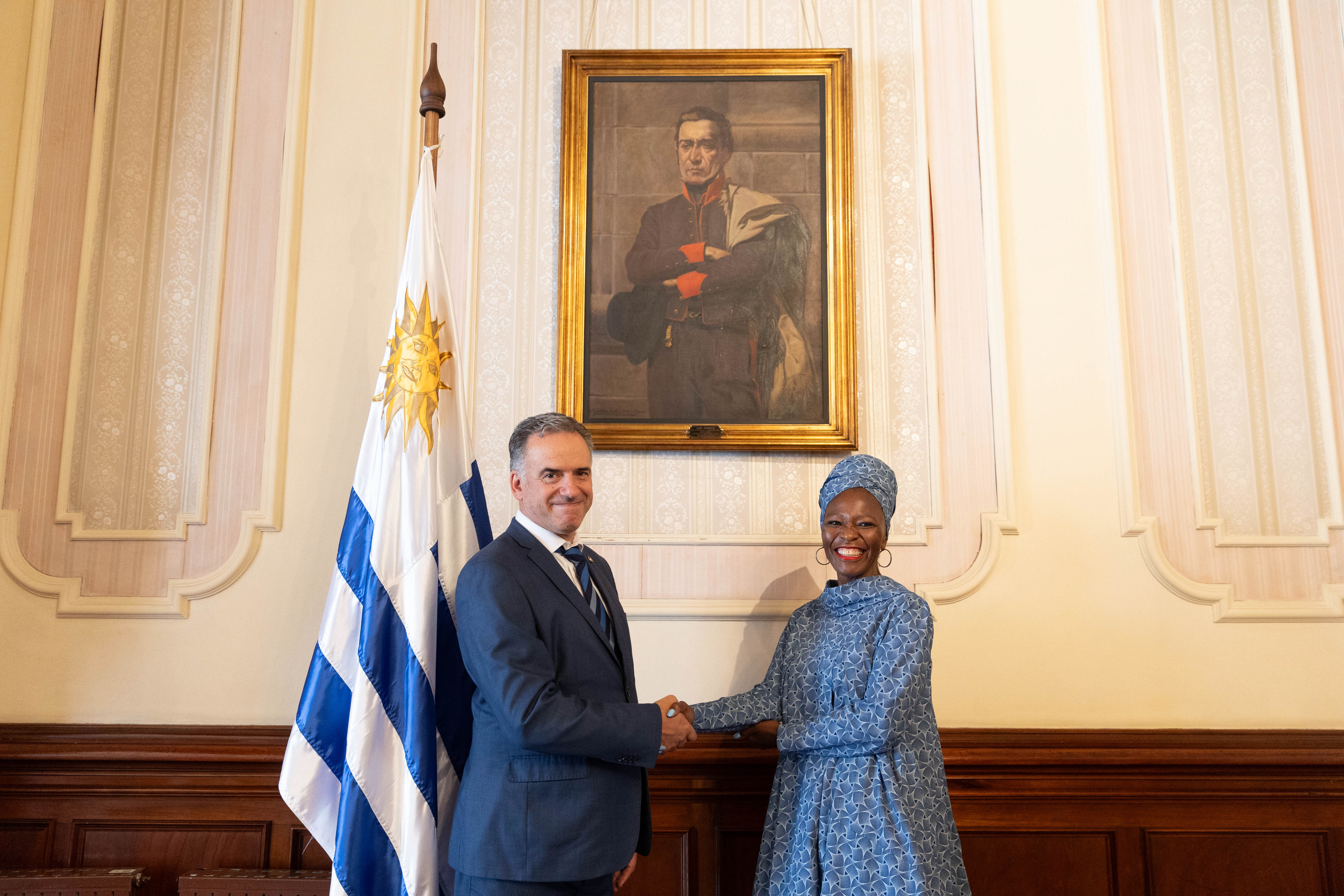 Orsi y embajadora de la República de Botsuana posan sonrientes frente a cámara mientras se estrechan las manos.
