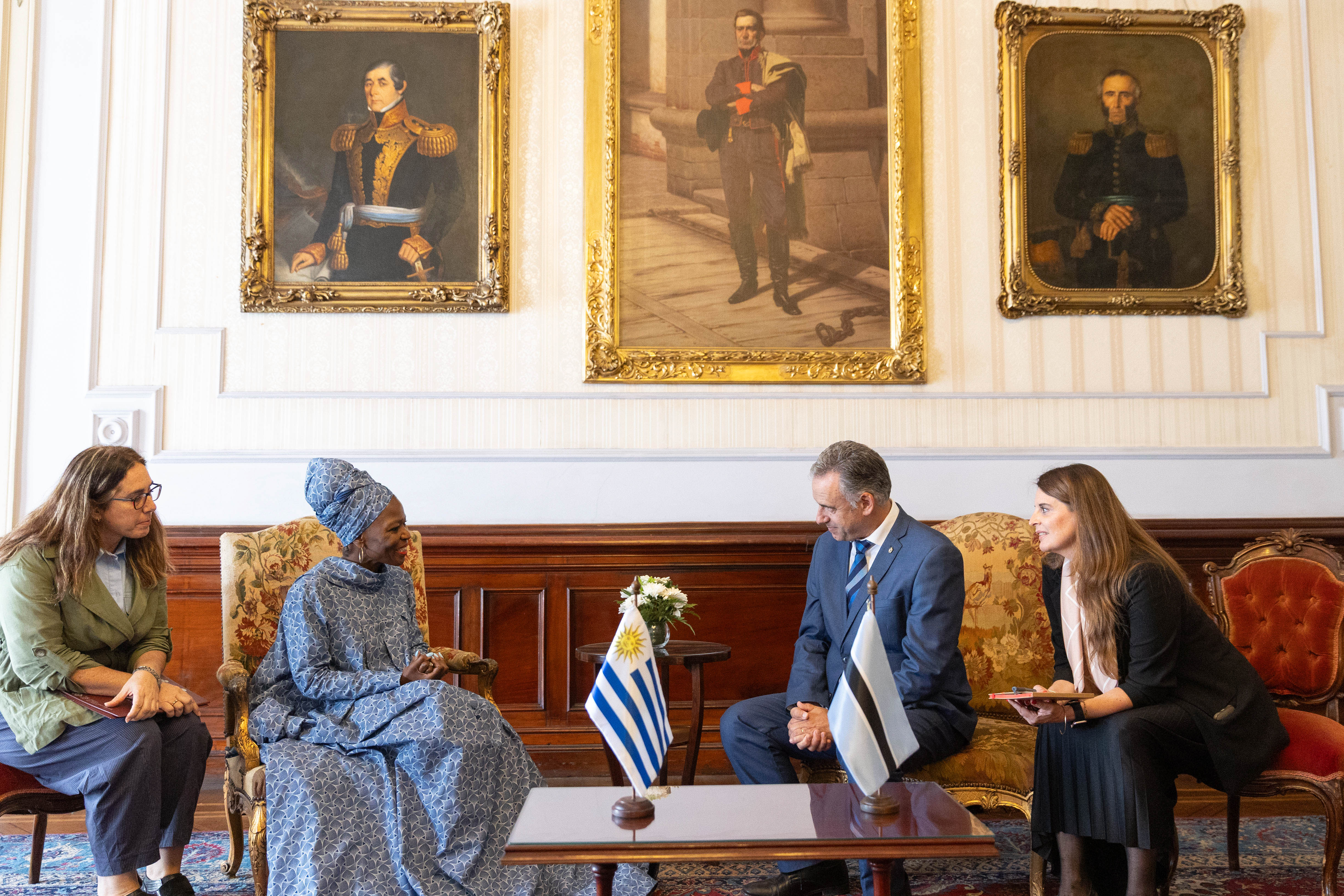 Orsi y embajadora de la República de Botsuana sentados en sillones dialogan entre sí. A sus costados dos traductoras los observan.