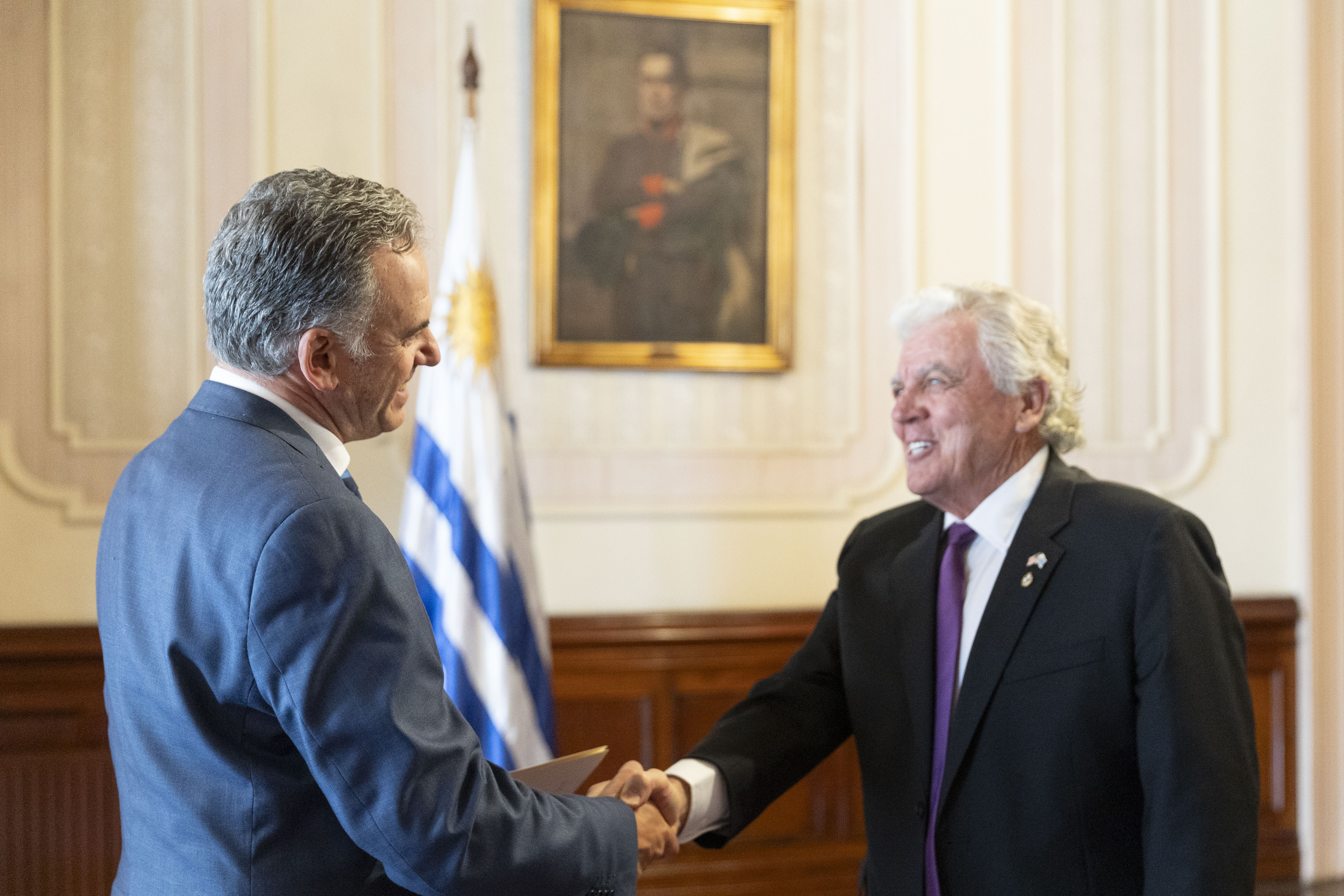 Orsi y embajador de Estados Unidos se estrechan las manos en el salón principal del palacio.