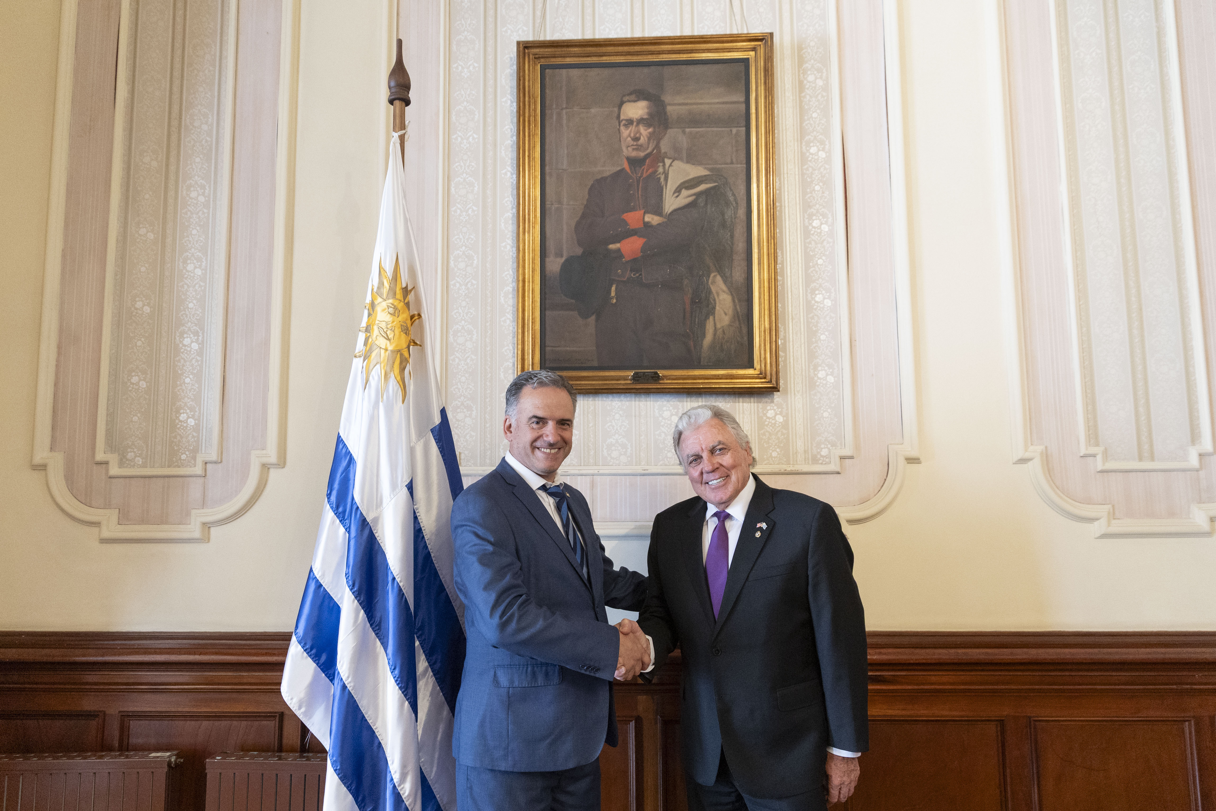 Orsi y embajador de Estados Unidos posan sonrientes frente a cámara mientras se estrechan las manos.
