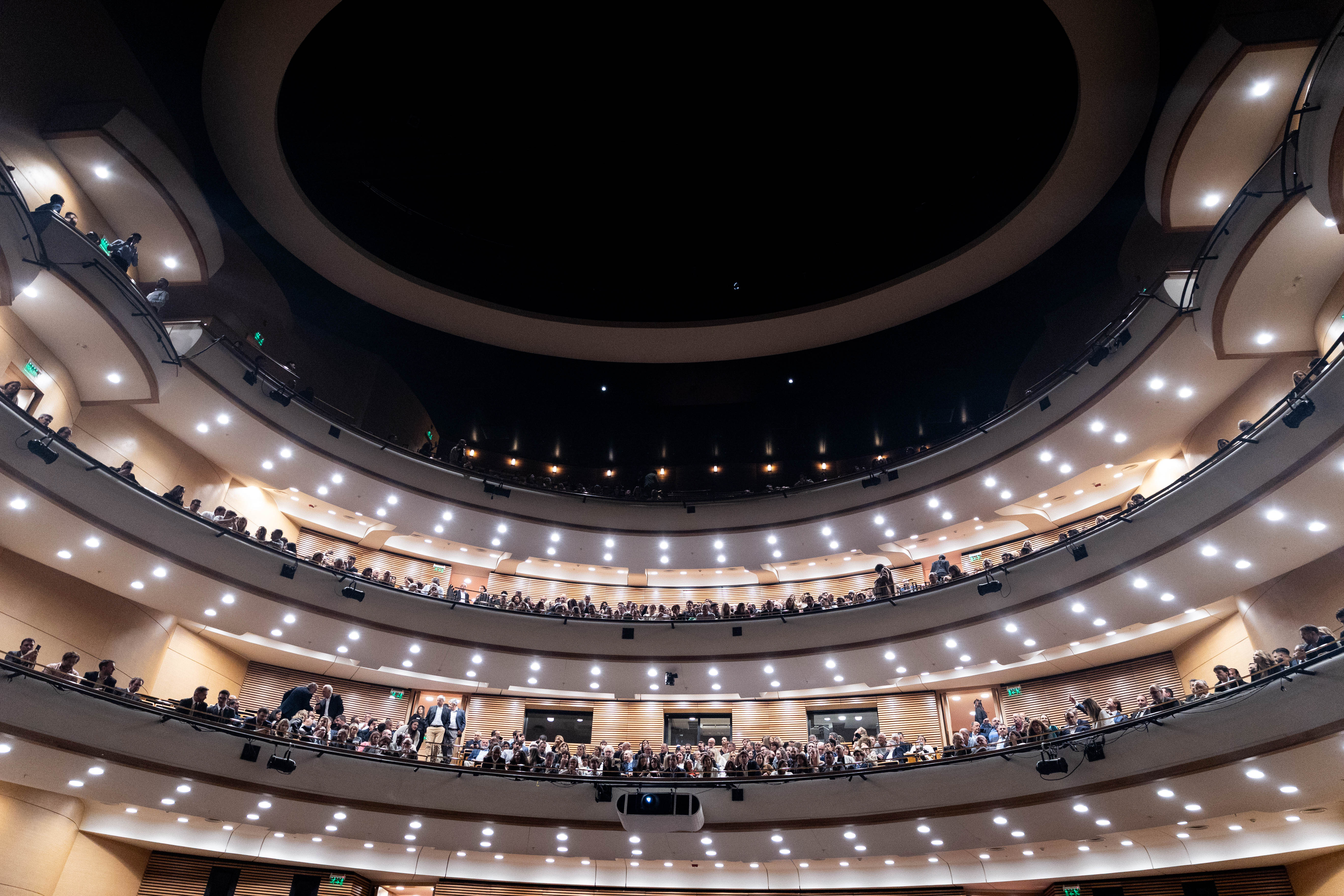 Vista desde abajo del auditorio Adela Reta con múltiples niveles de balcones, en forma circular, llenos de gente y un gran techo oscuro.