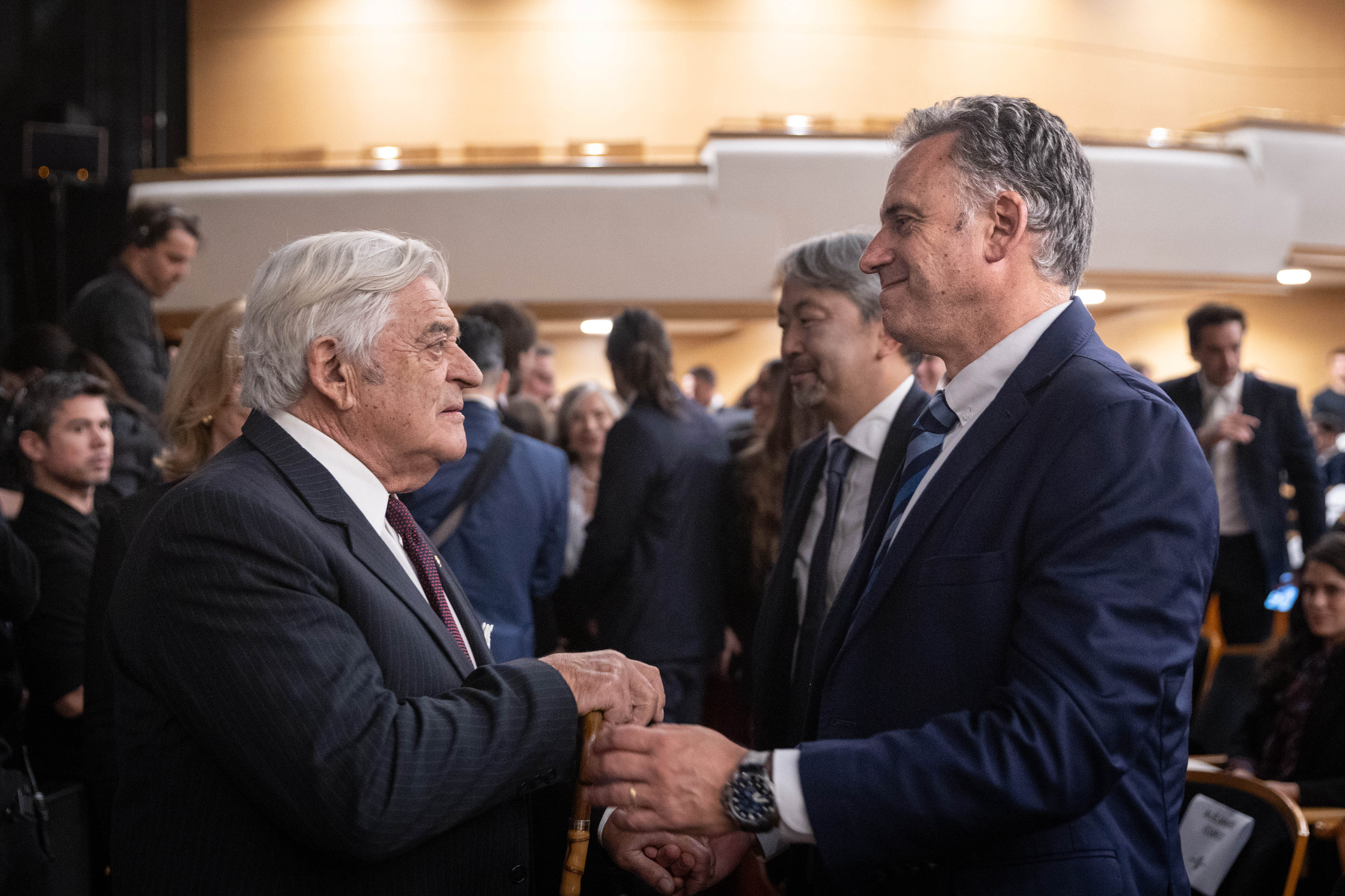Orsi saluda al expresidente Lacalle Herrera en la platea del auditorio Adela Reta. A su alrededor hay varios asistentes al evento.