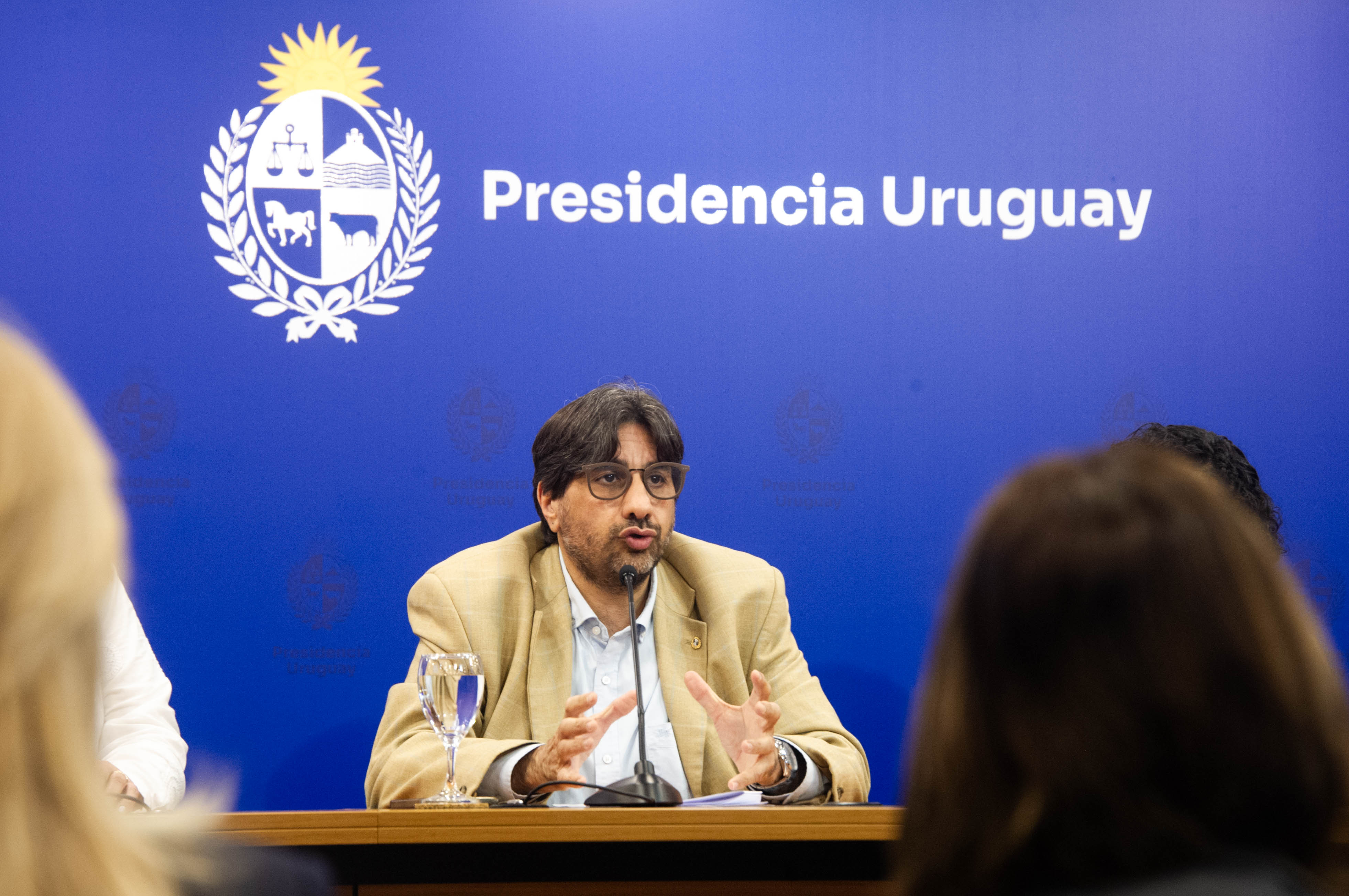 Presidente de la Unasev diserta sentado en mesa con micrófono mientras el público, de espaldas, lo observa.