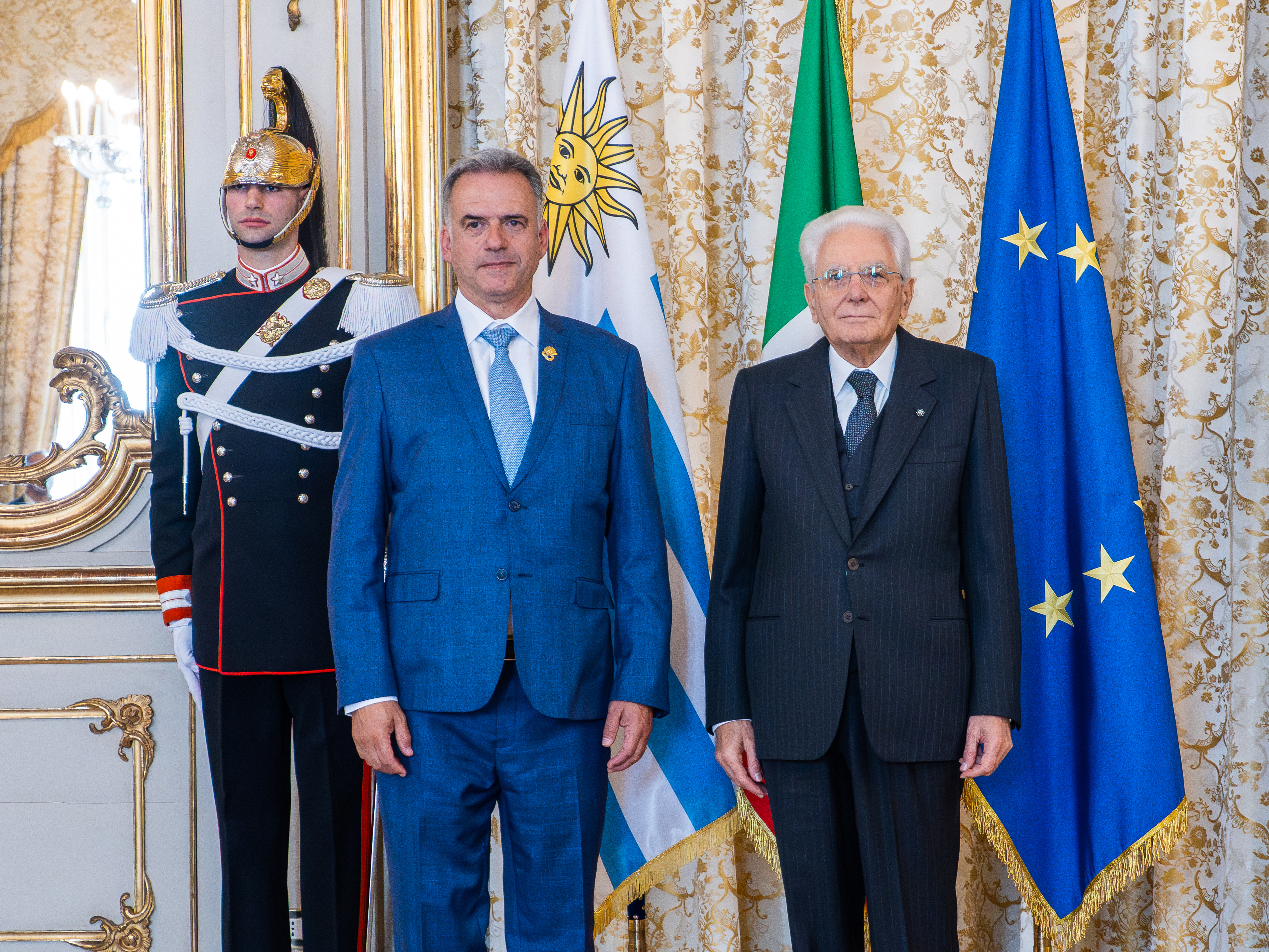 Los presidentes de Uruguay e Italia, de pie, posan para una foto. Atrás se observa un custodio presidencial y banderas de ambos países. 