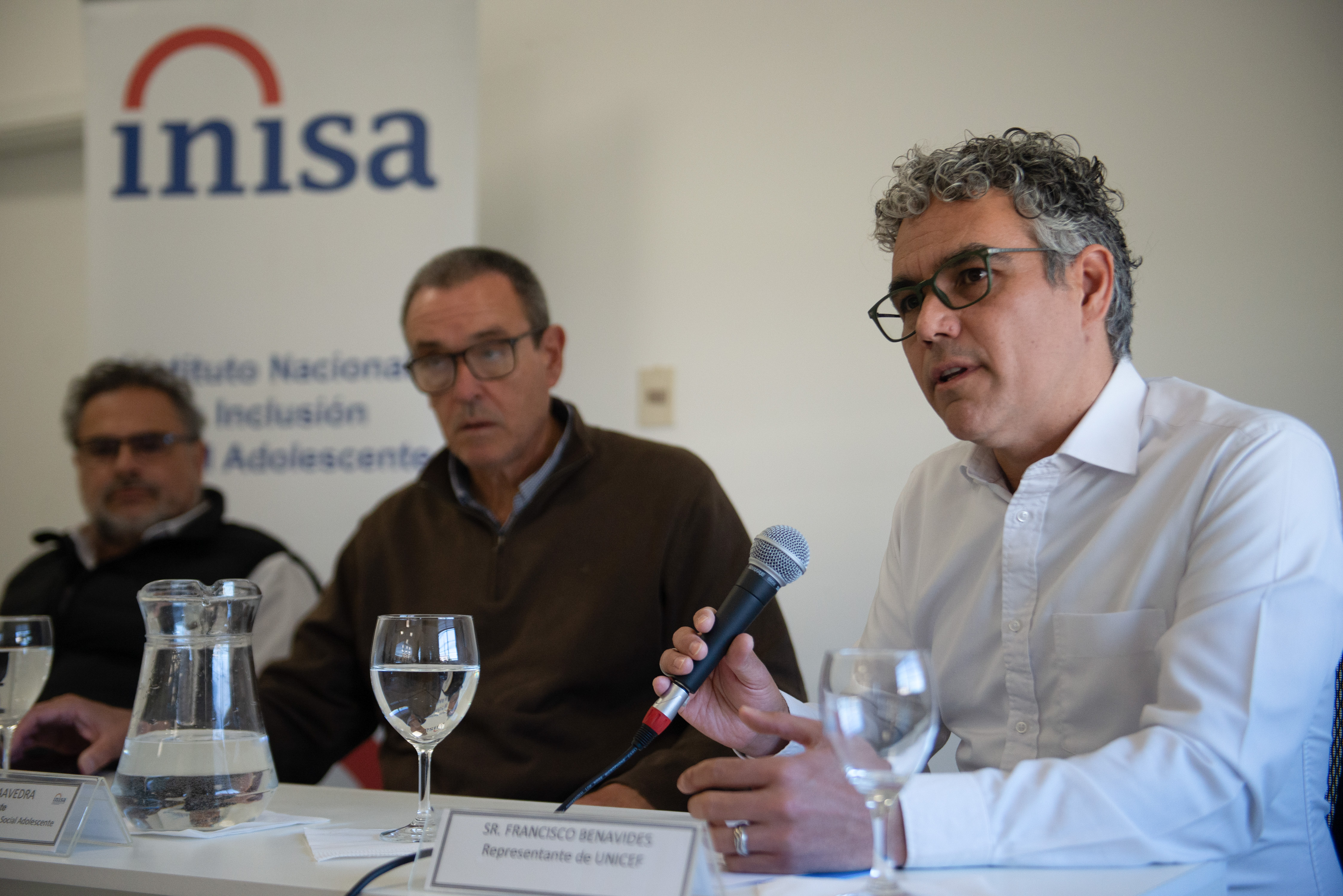 Representante de Unicef Uruguay diserta en una mesa frente a un micrófono, a su lado están el presidente y el director del Inisa.