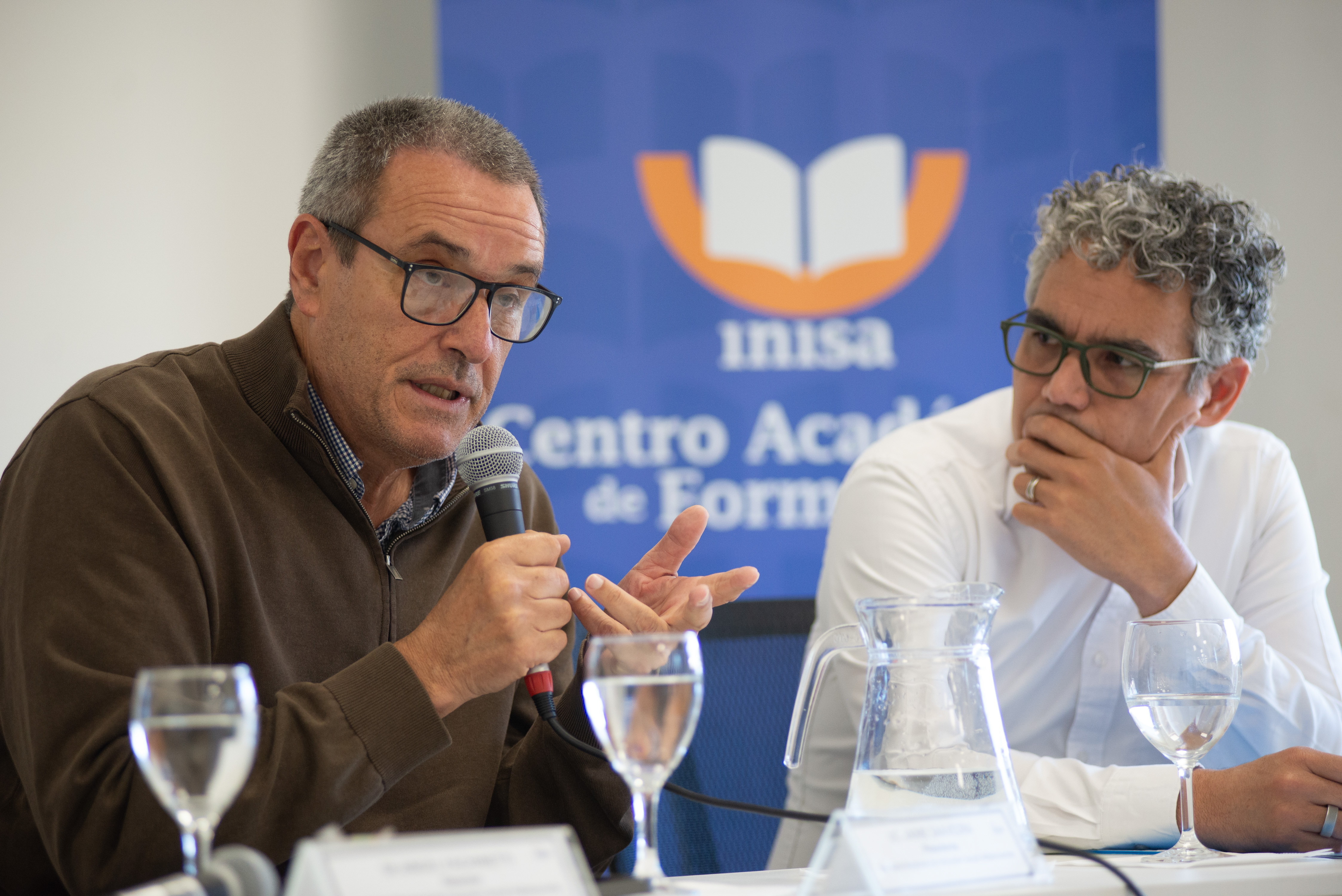 Presidente del Inisa diserta con micrófono en mano. A su lado el representante de Unicef Uruguay lo observa.