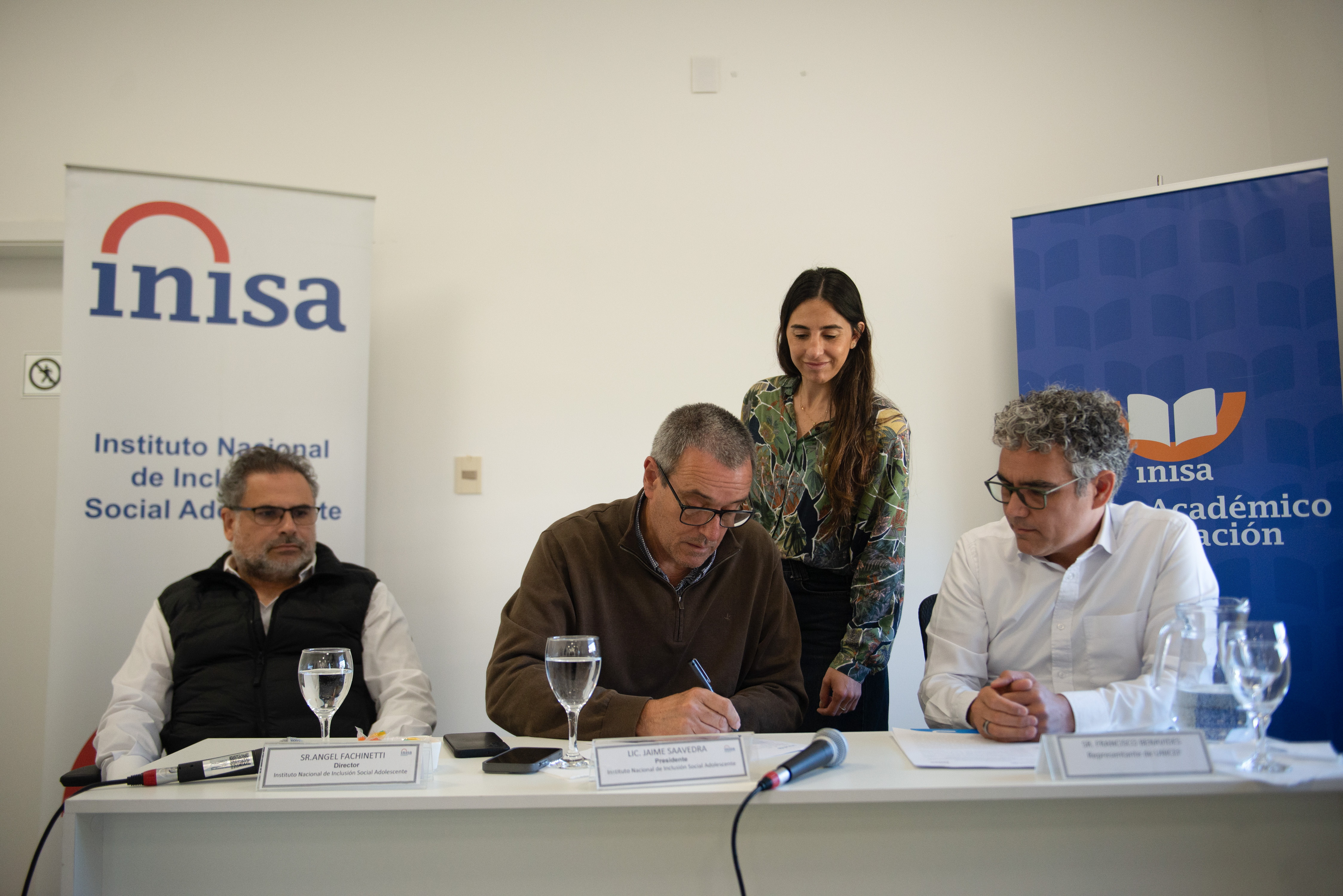 Presidente de Inisa firma un papel sobre una mesa mientras las demás autoridades lo observan.