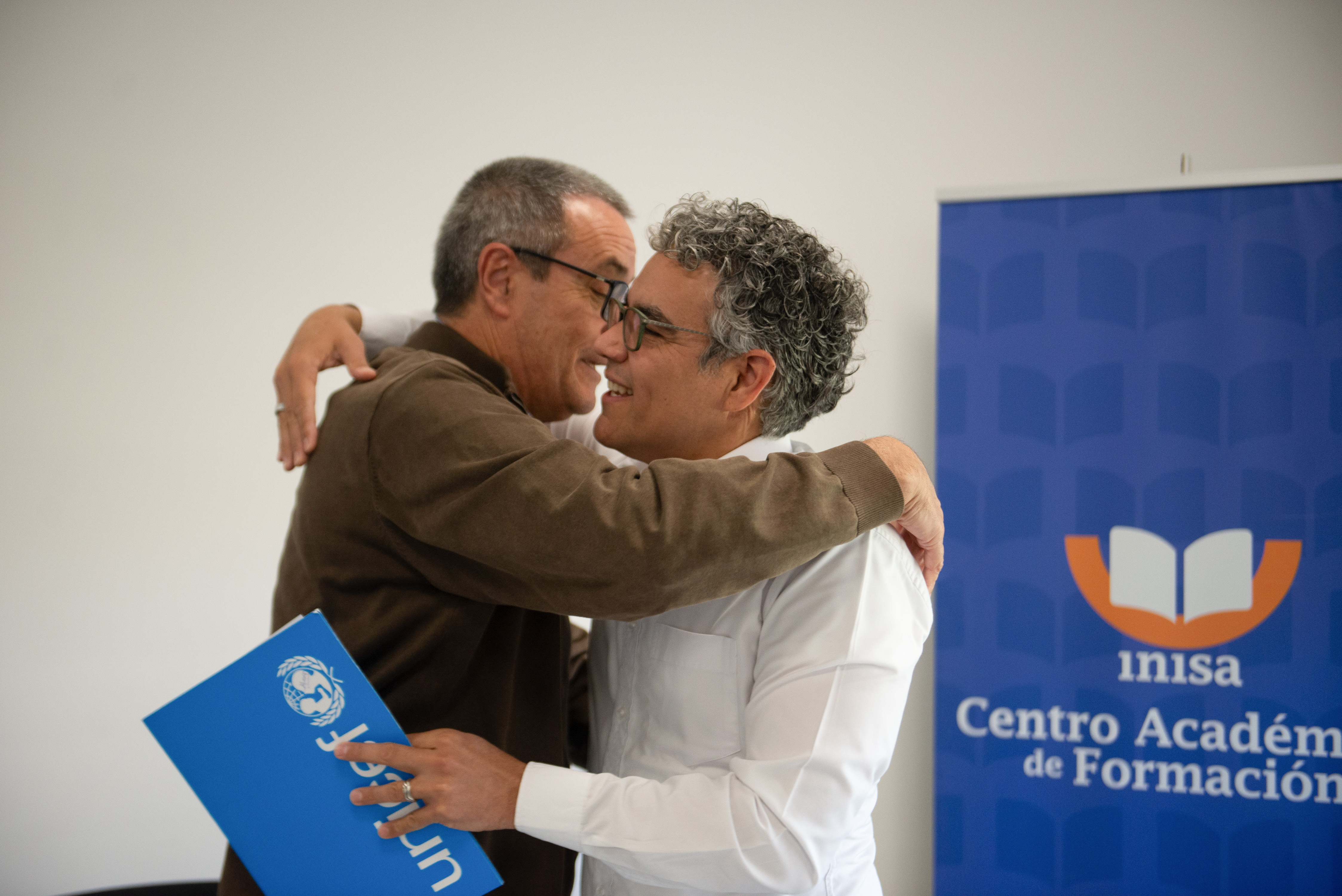 Presidente del Inisa y el representante de Unicef Uruguay se abrazan. Atrás se observa cartel azul con logo de Inisa.