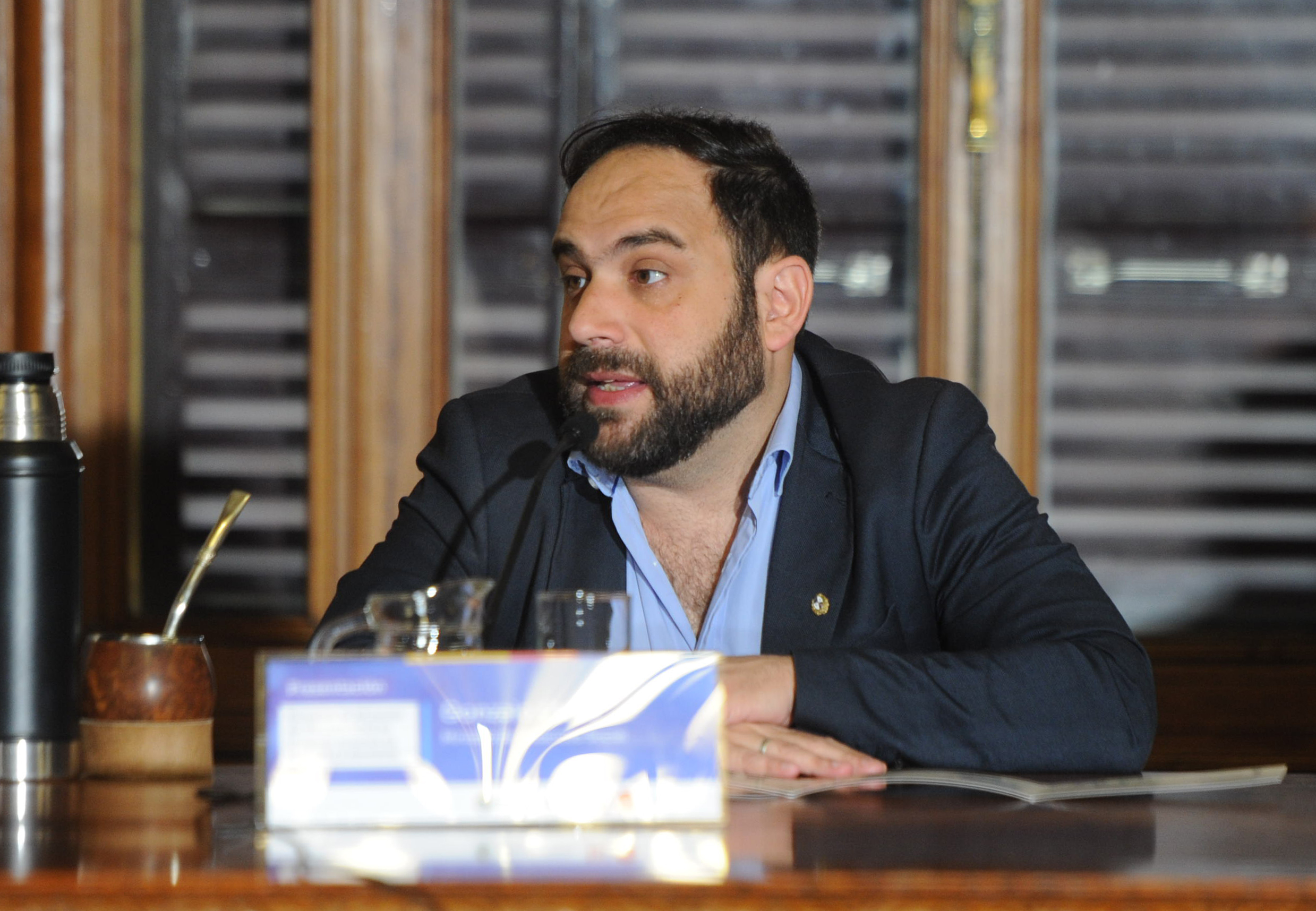 Titular del Ministerio de Desarrollo Social diserta, sentado en mesa de madera, del salón de eventos especiales del Palacio Legislativo.