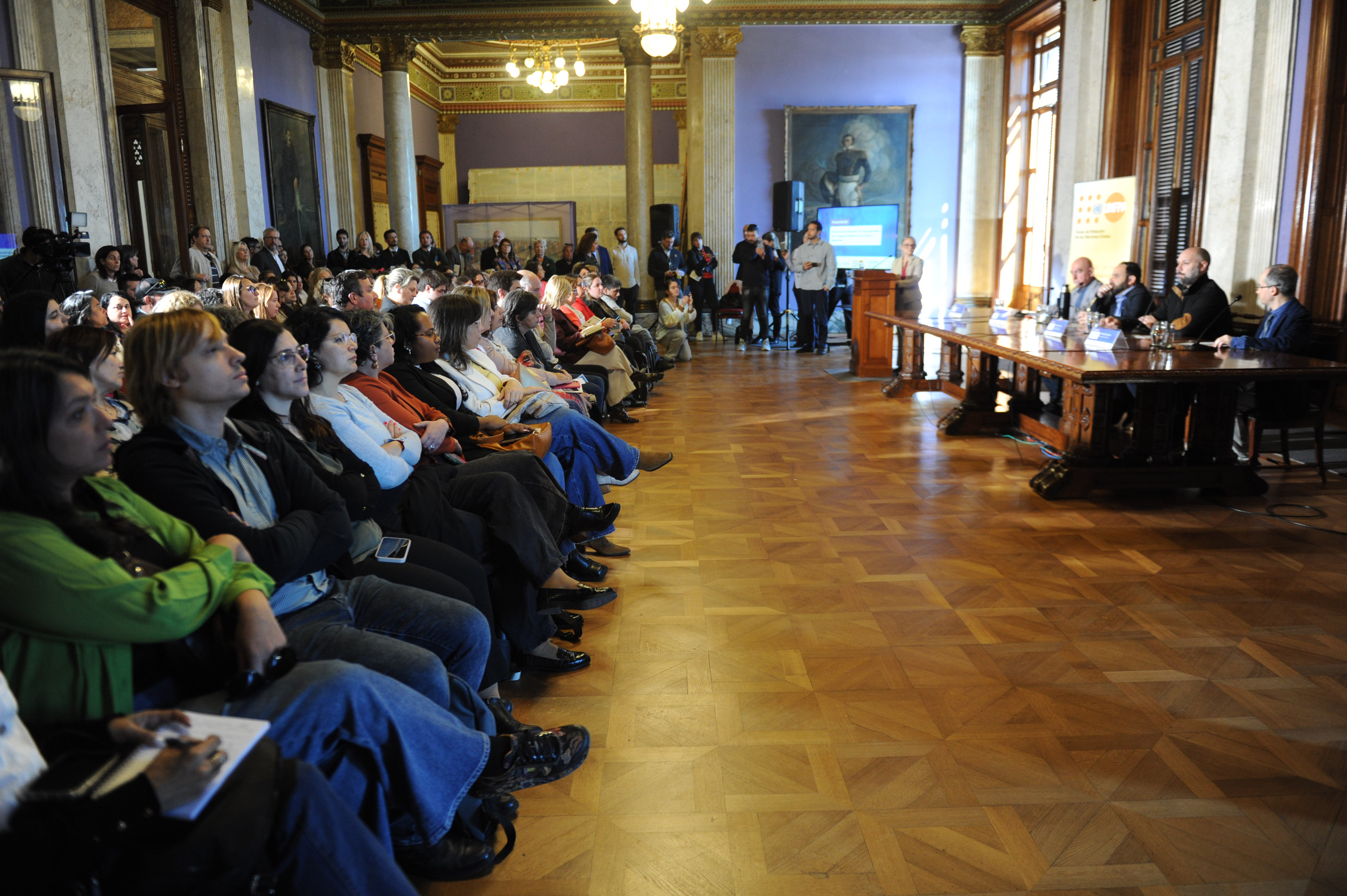 Desde una perspectiva de costado se ve la mesa con autoridades y el público sentado observado.