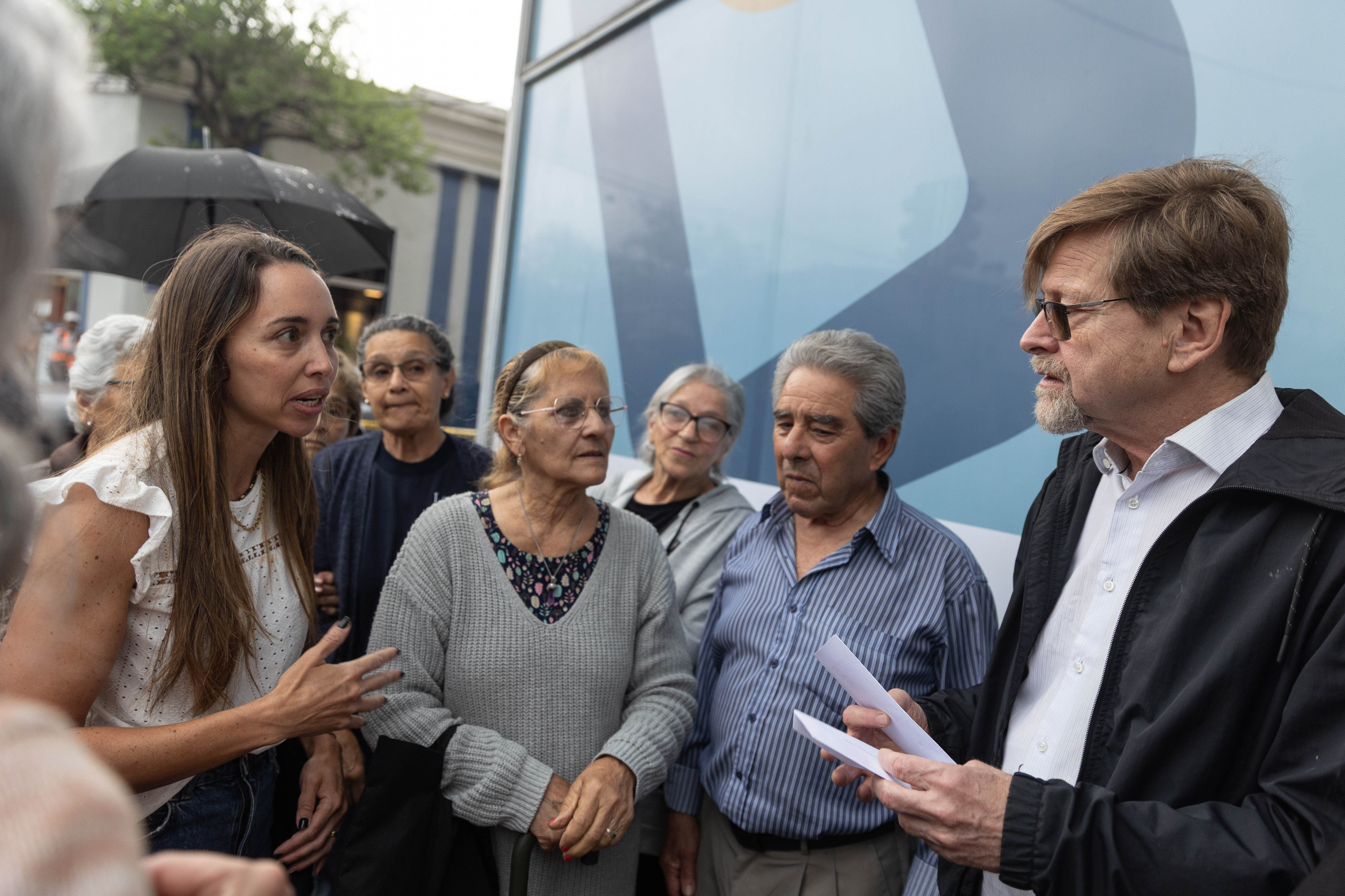 Un hombre y una mujer dialogan al aire libre mientras otras personas los observan.