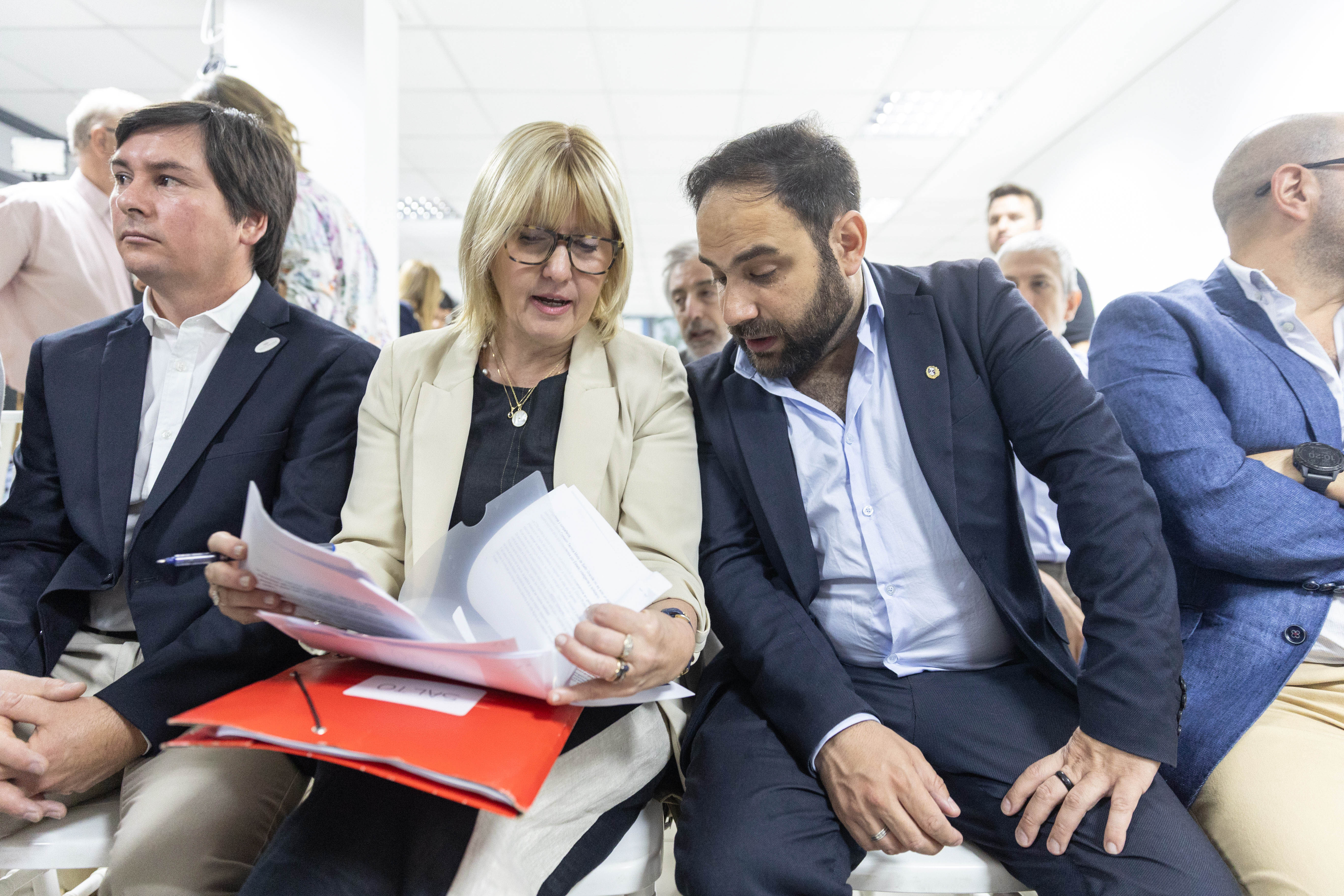 Los ministros de Desarrollo Social y Salud Pública, sentados en la platea entre el público, revisan unos documentos juntos.