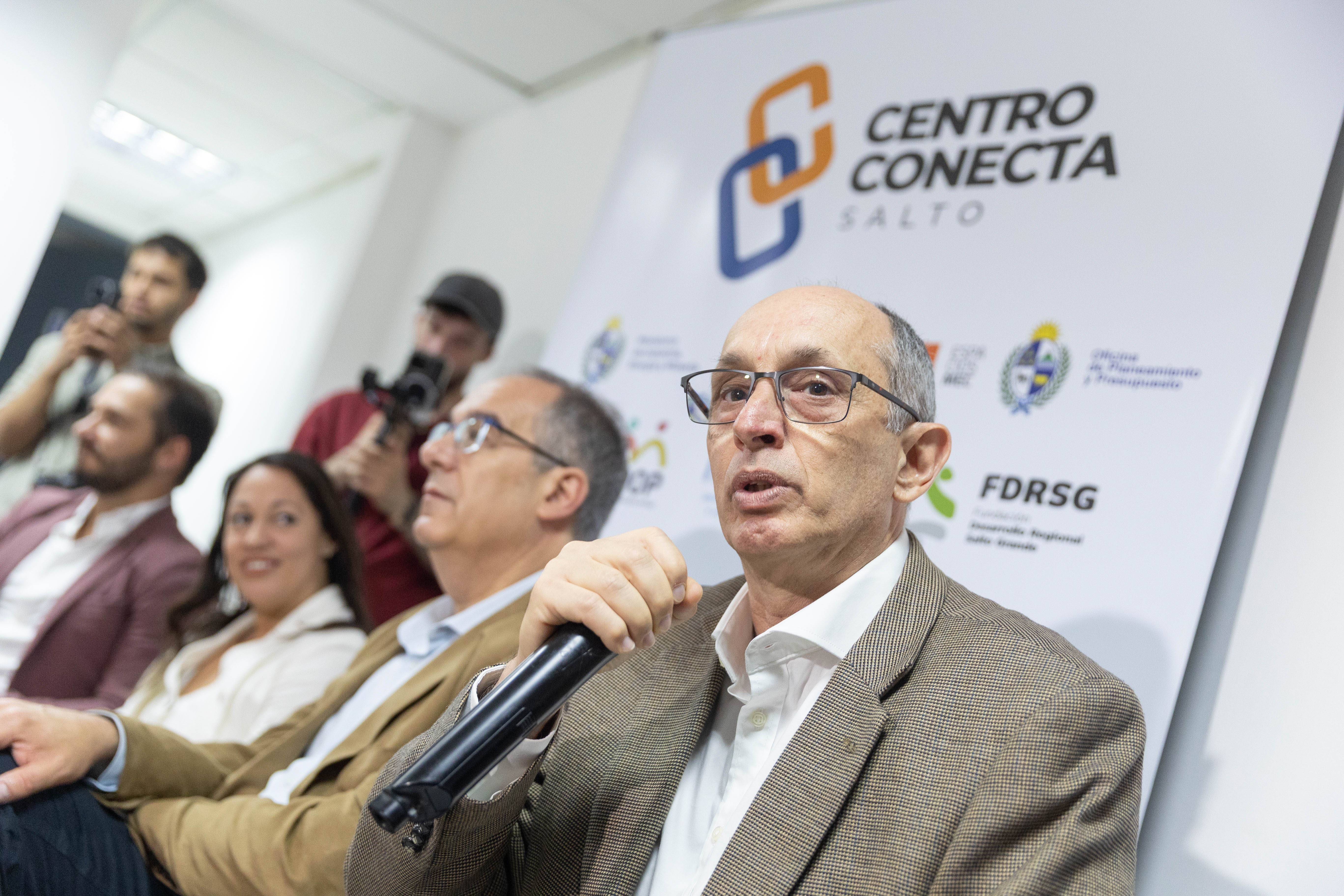 El presidente de la CTM por Uruguay diserta sentado en mesa con micrófono en mano, mientras las demás autoridades lo observan.