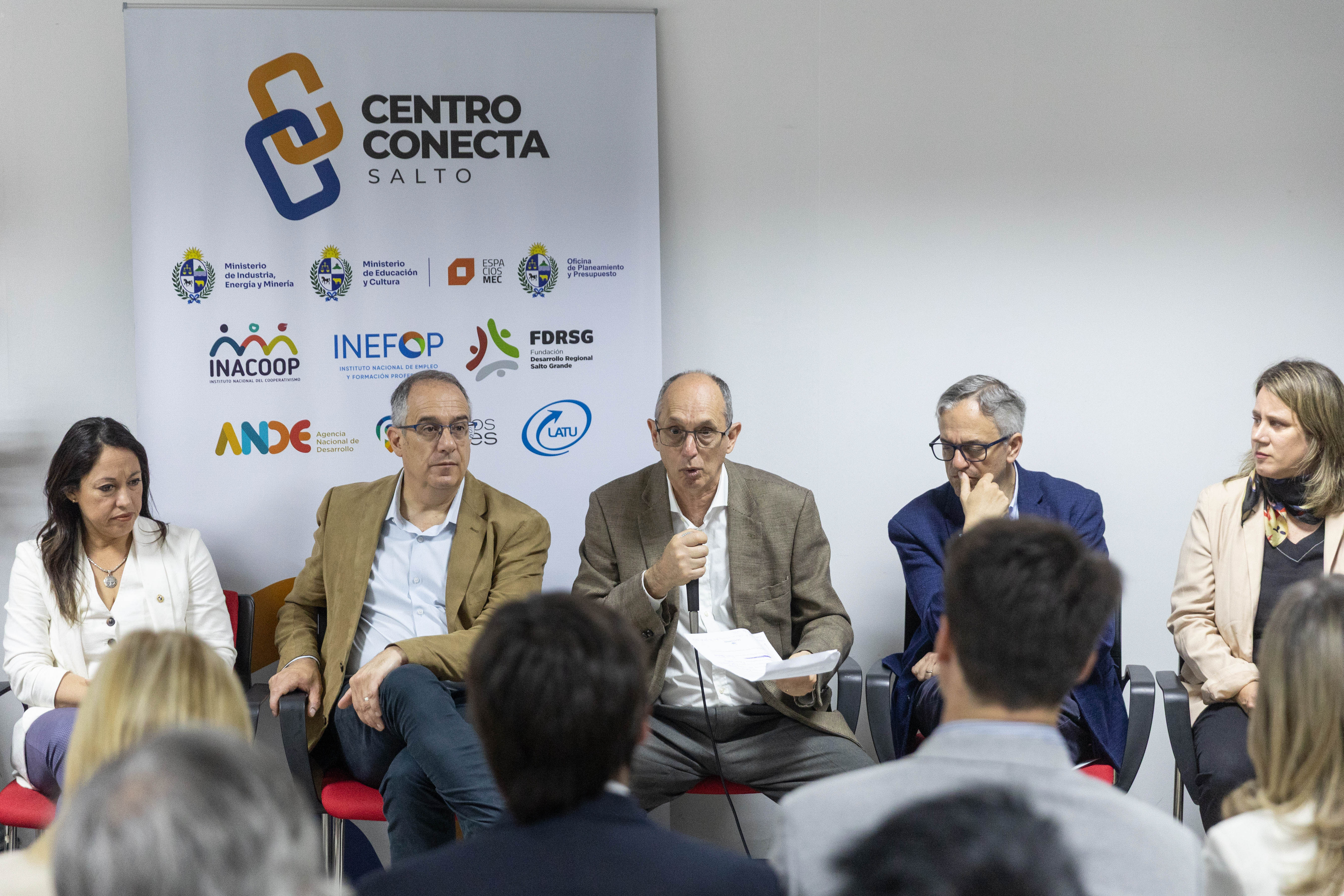 Otra perspectiva del presidente de la CTM disertando sentado en mesa con micrófono en mano, mientras las demás autoridades lo observan.