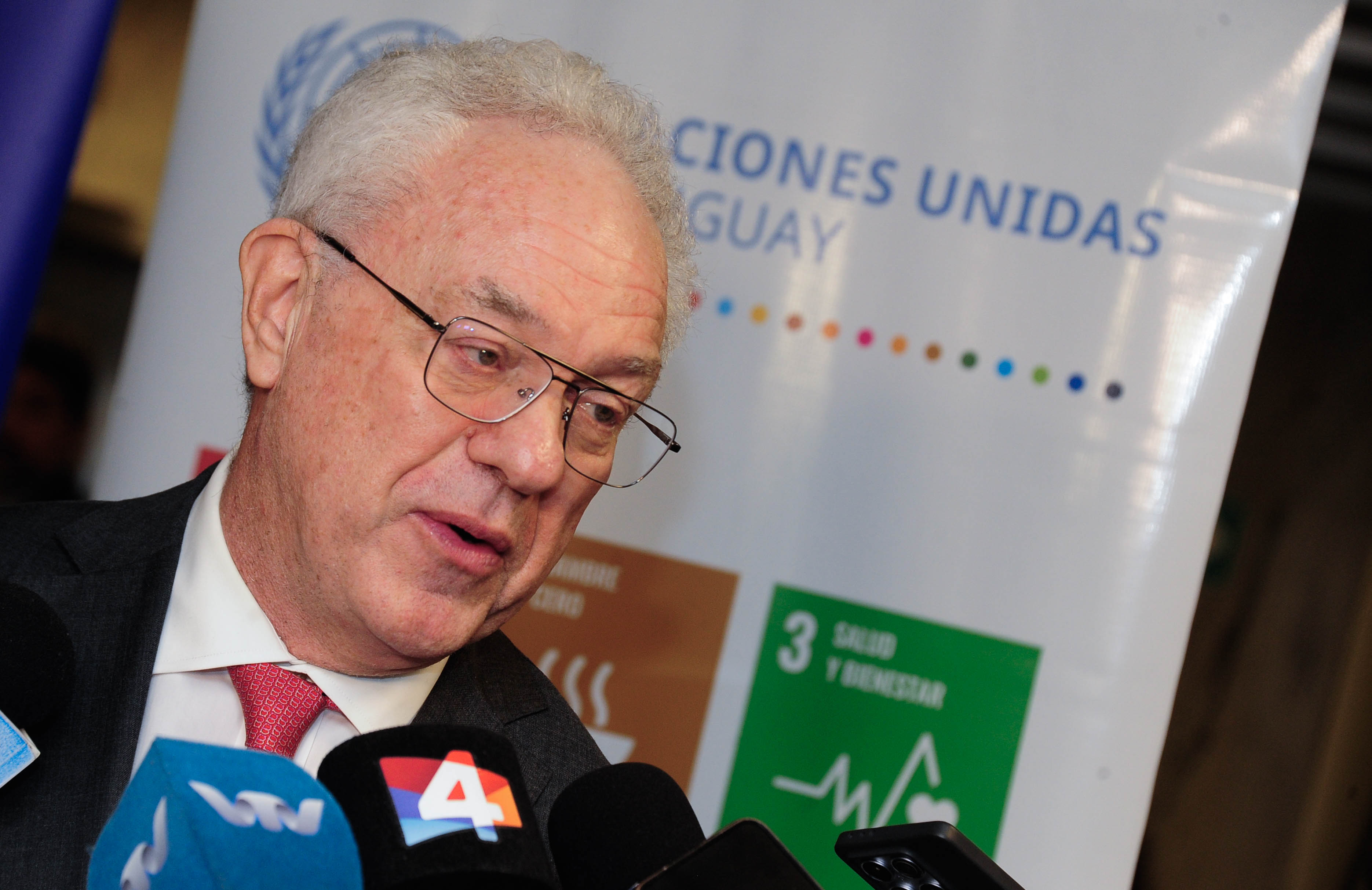 El canciller uruguayo dialoga con periodistas frente a varios micrófonos de prensa. Atrás cartel colorido con logo de la ONU.