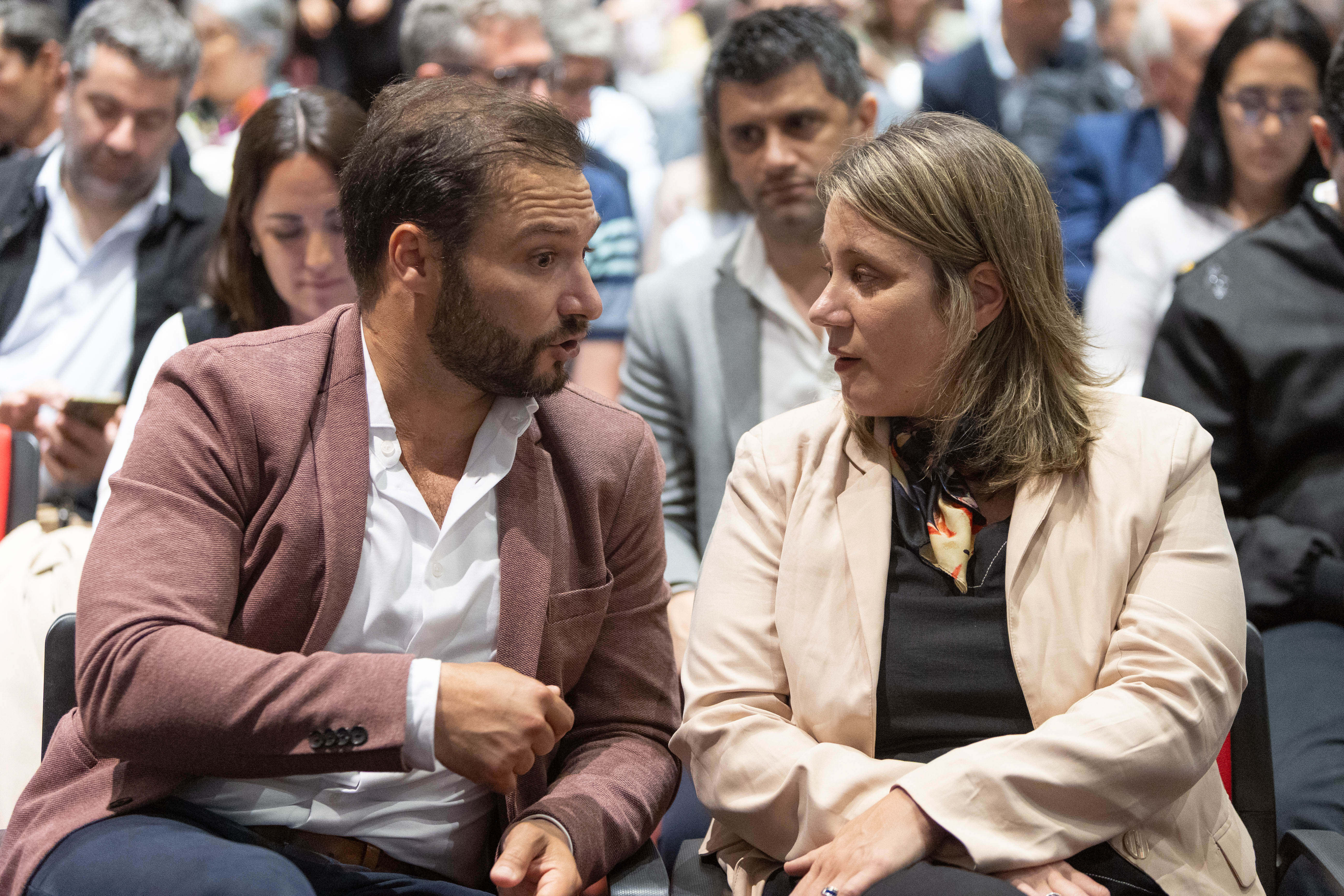 Presidente de ANDE y vicepresidenta de Inacoop conversan sentados en la platea entre el público.