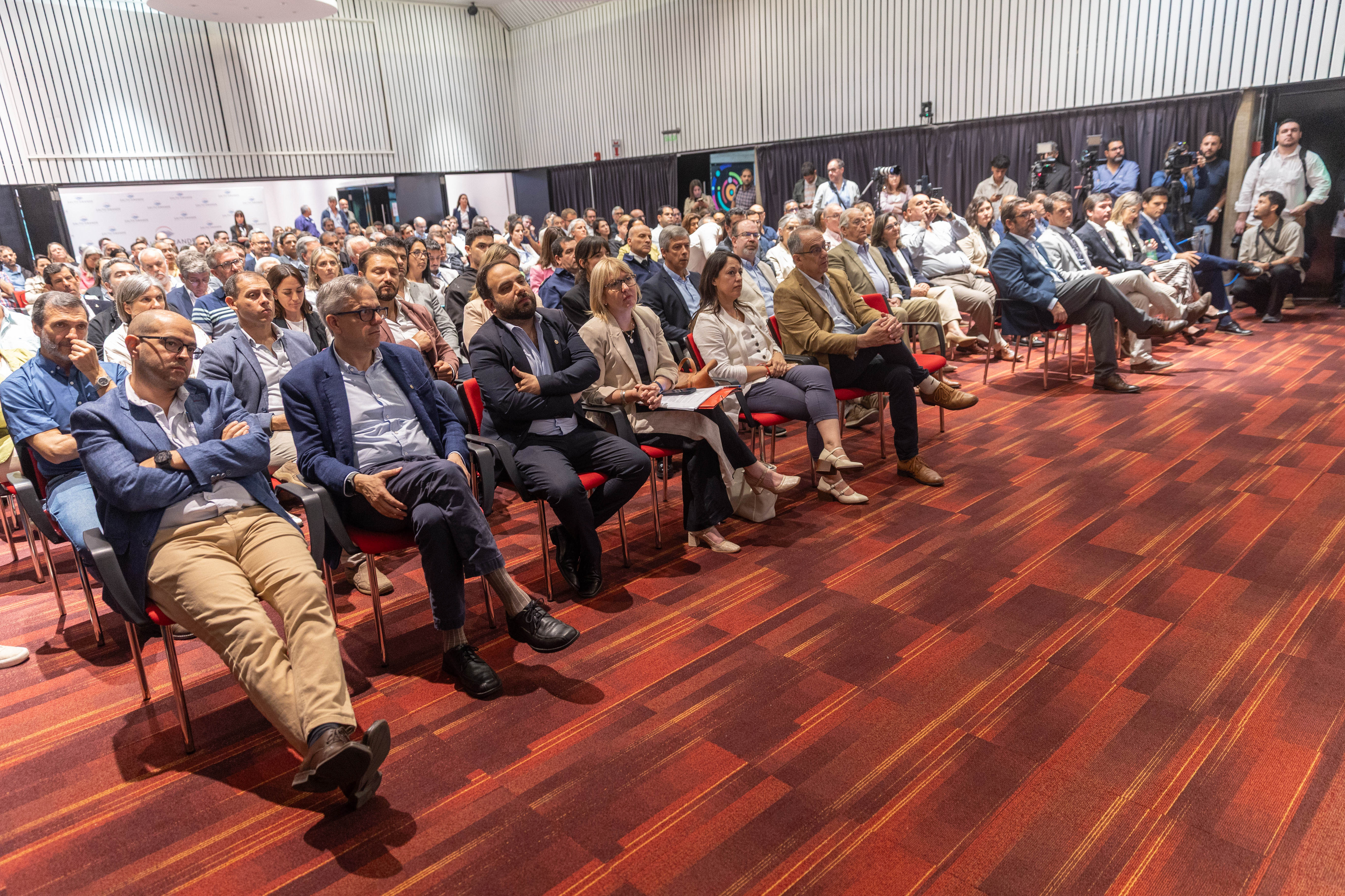 Plano general del salón de actos con el público sentado en la platea escuchando una disertación.