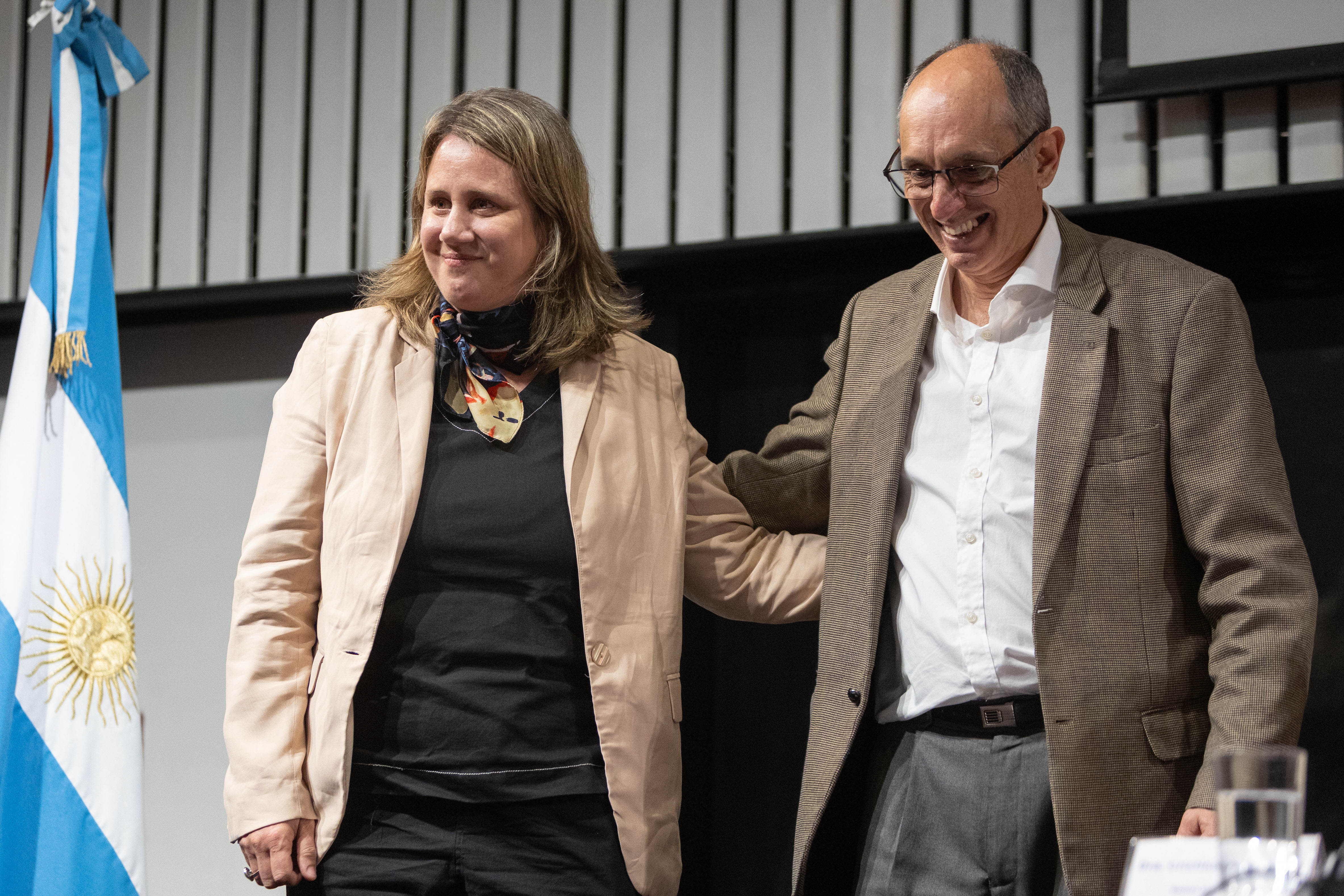 El presidente de la CTM por Uruguay y la vicepresidenta de Inacoop sonríen abrazados en el escenario.