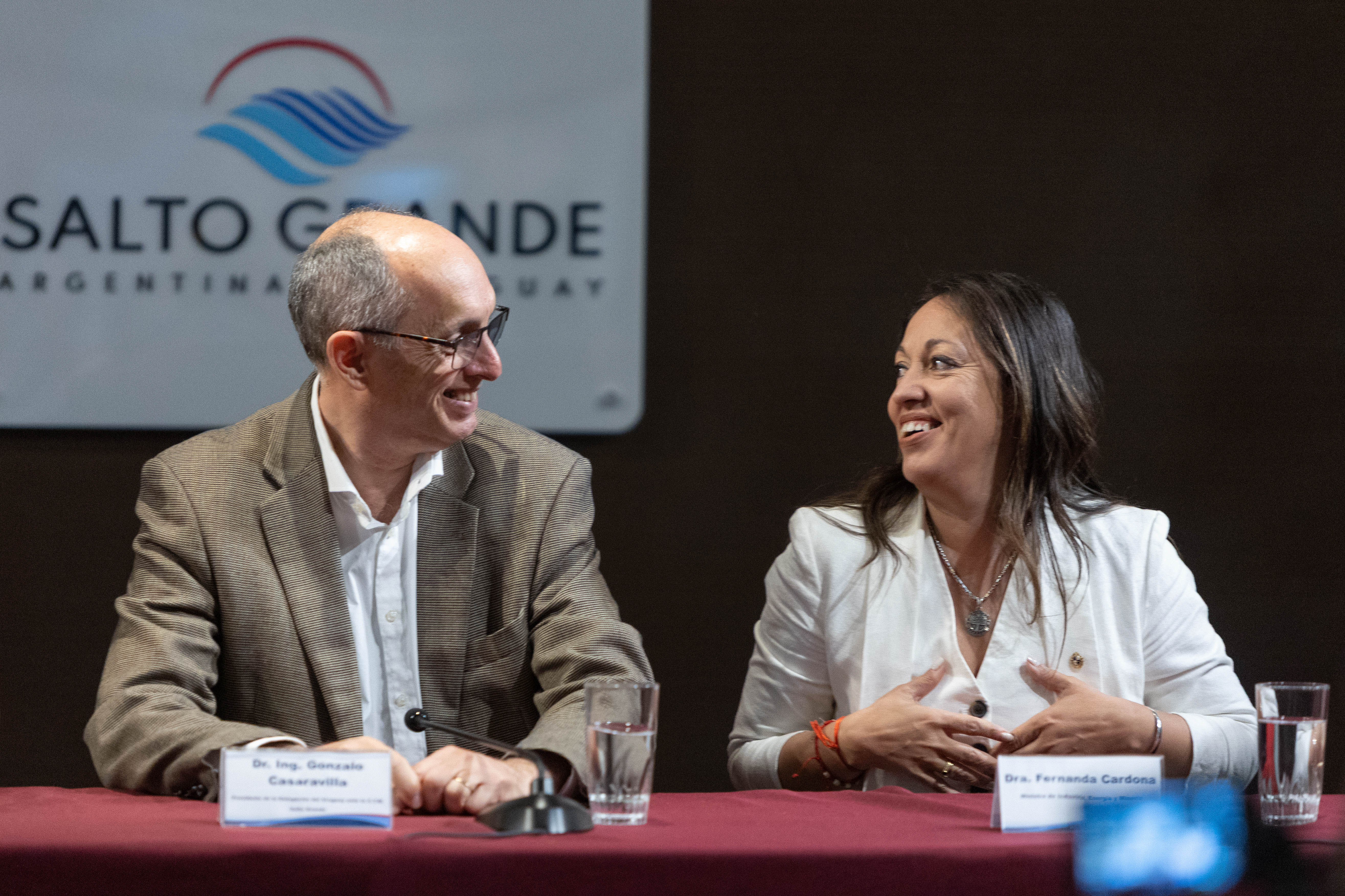 La ministra de Industria y el presidente de la CTM por Uruguay sonríen mientras conversan sentados en mesa con micrófonos.