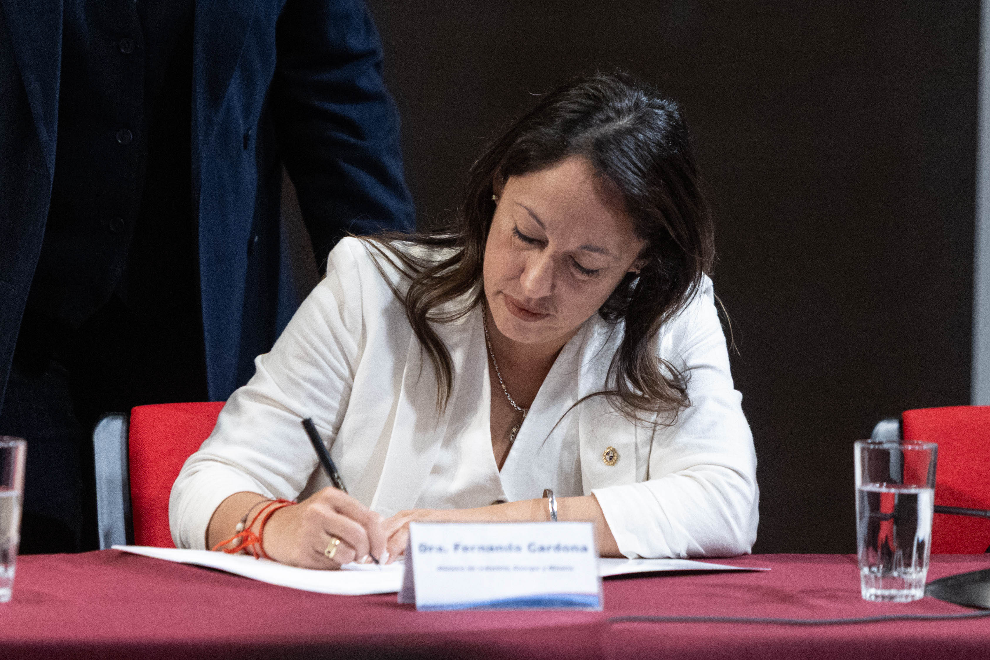Primer plano de la ministra de Industria, sentada en mesa, firmando unos documentos.