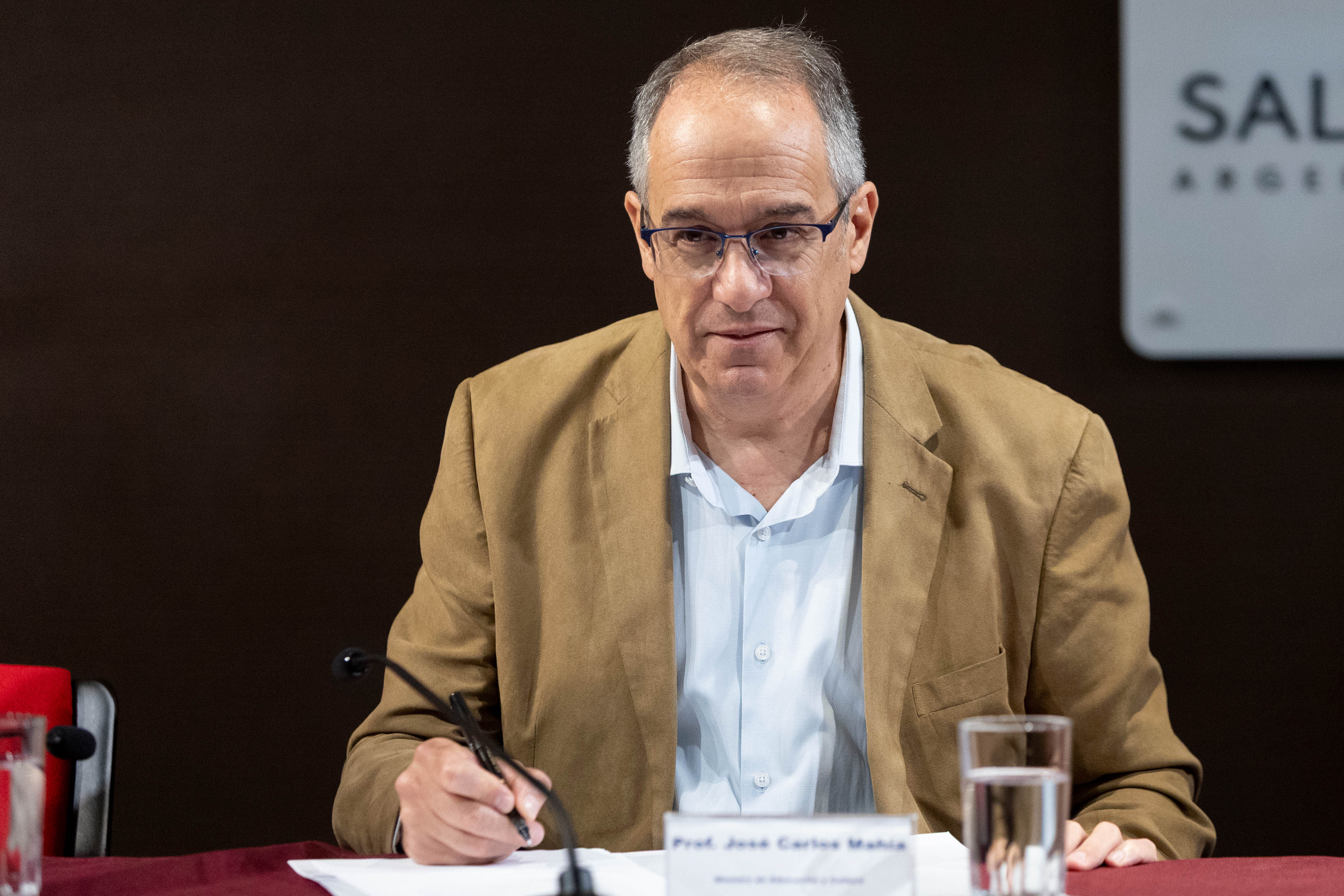 Primer plano del ministro de Educación y Cultura, sentado en mesa, firmando unos documentos.