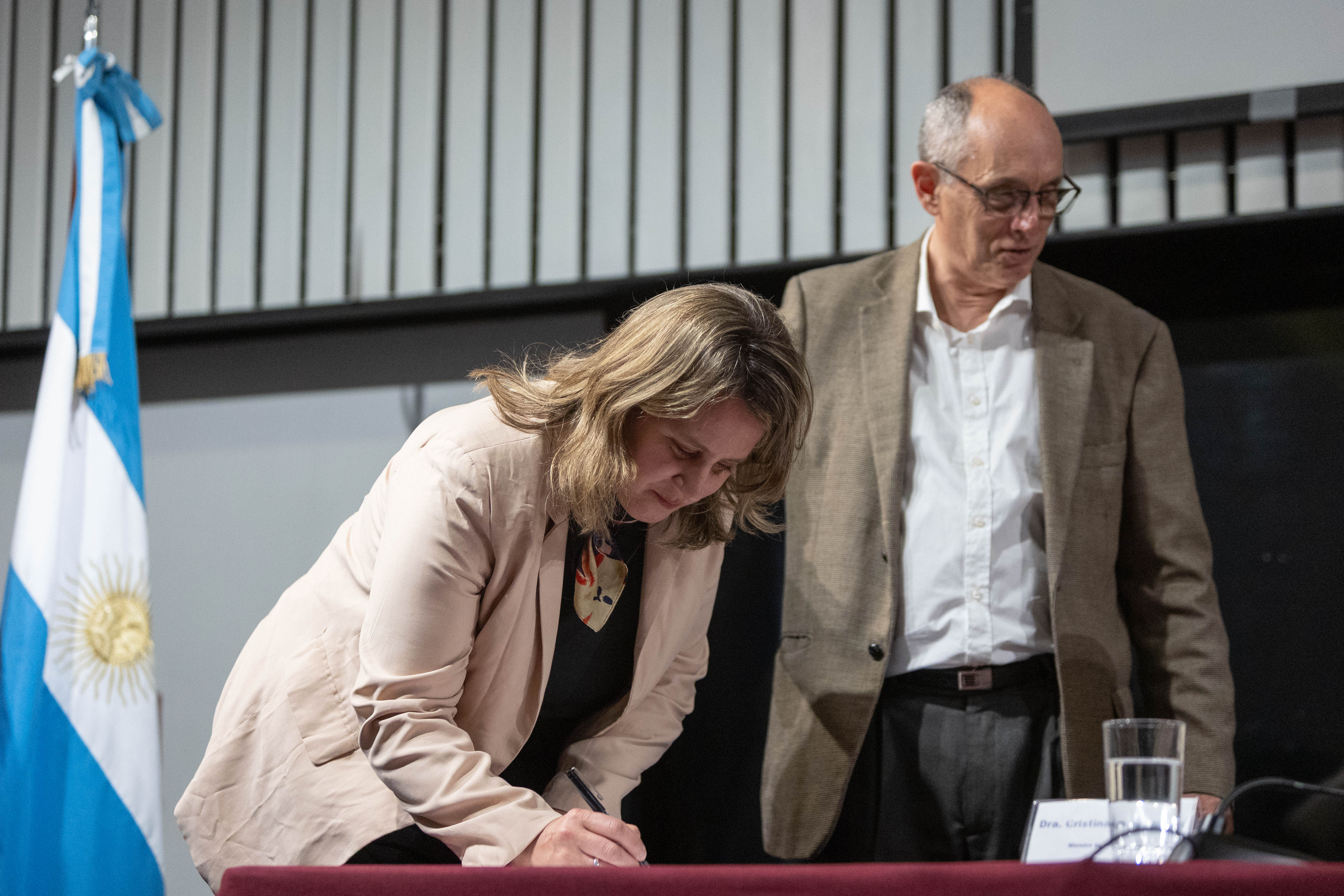 La vicepresidenta de Inacoop firma unos documentos sobre una mesa. Atrás está el presidente de la CTM por Uruguay.