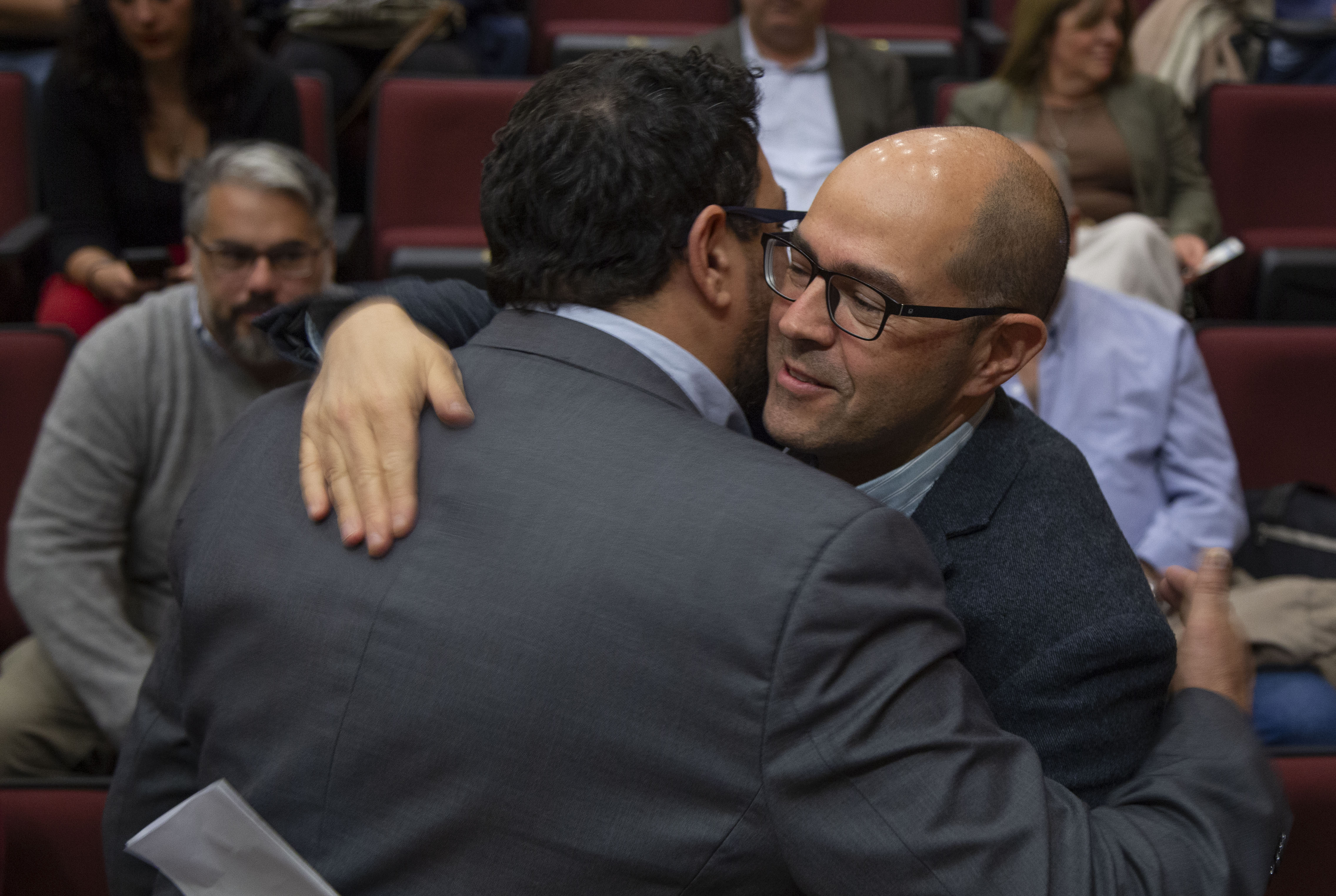 Secretario de Presidencia y presidente de la Administración de los Servicios de Salud del Estado se abrazan en la platea del auditorio.