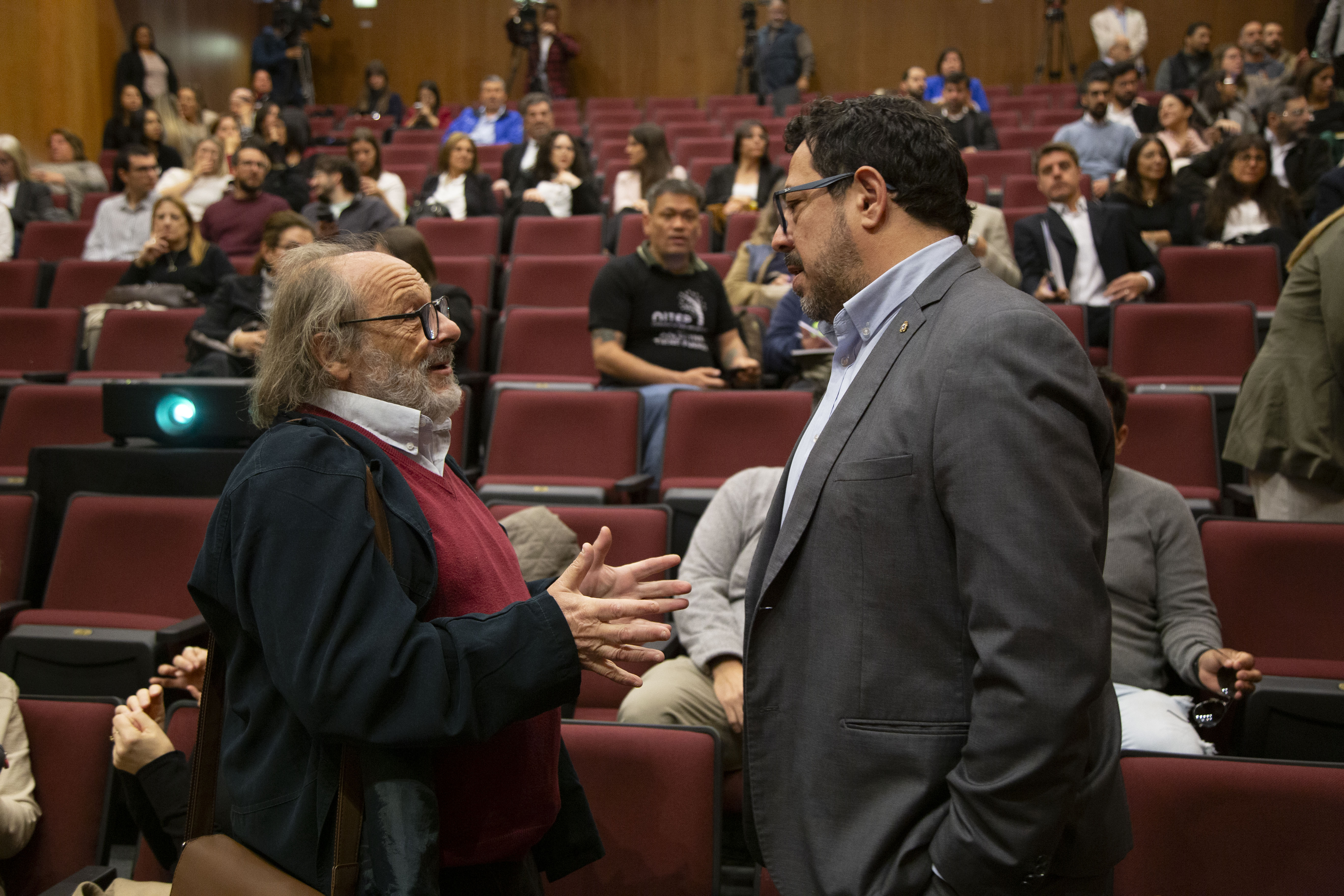 Vicepresidente de la ASSE y secretario de Presidencia dialogan, de pie, en la platea del auditorio.