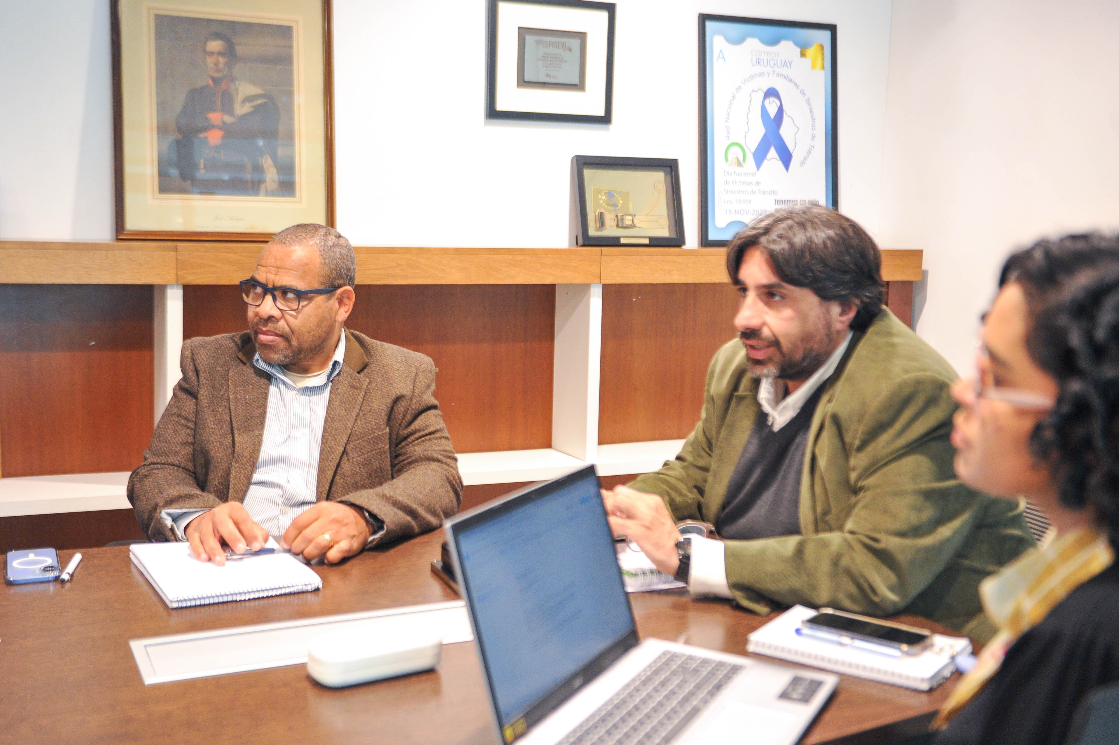 Presidente y autoridades de Unasev sentados en la mesa con una computadora portátil miran hacia un lado escuchando una disertación.