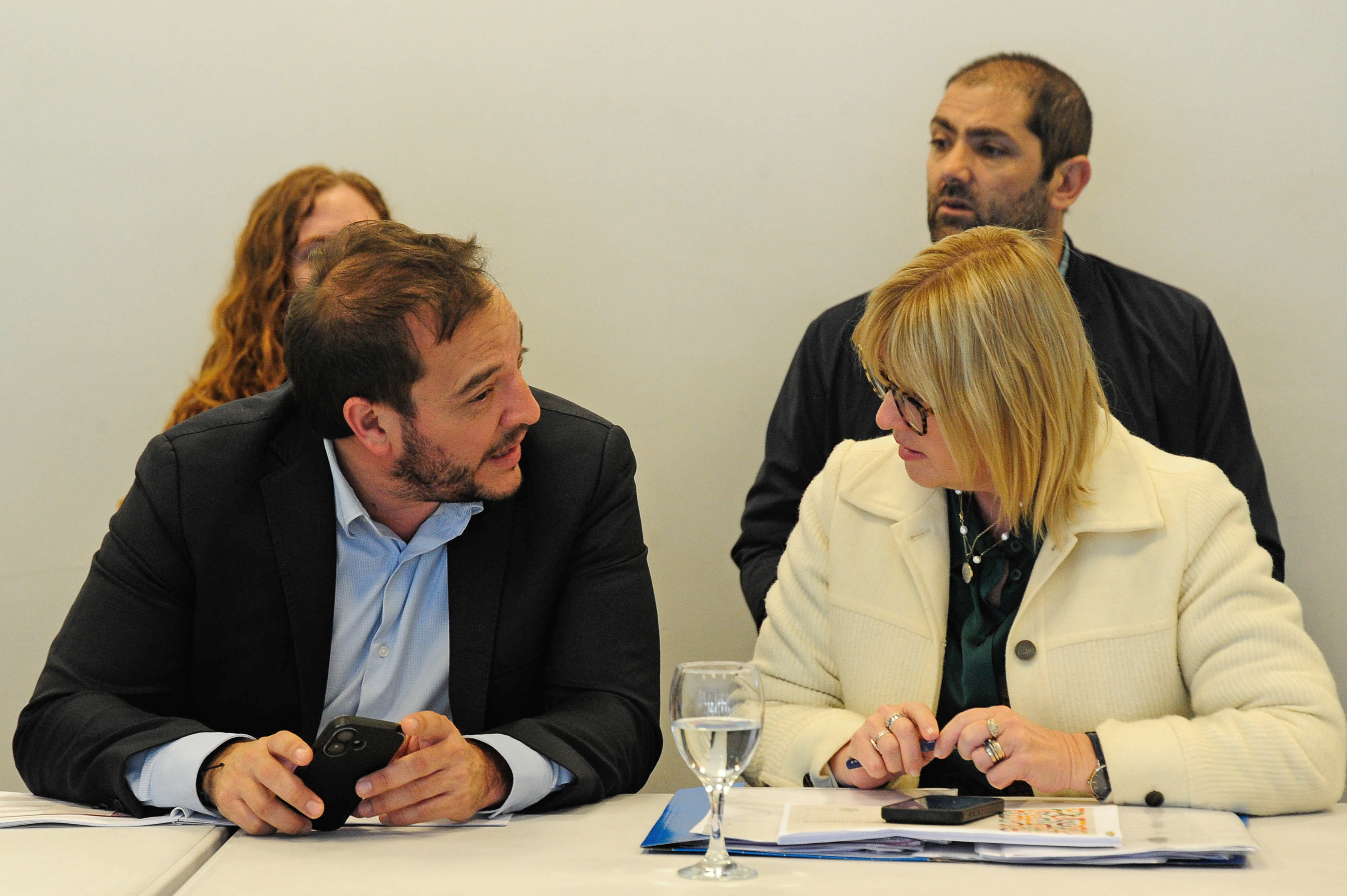 Subsecretario de Vivienda sentado conversa con la ministra de Salud Pública. Atrás dos personas sentadas los observan.