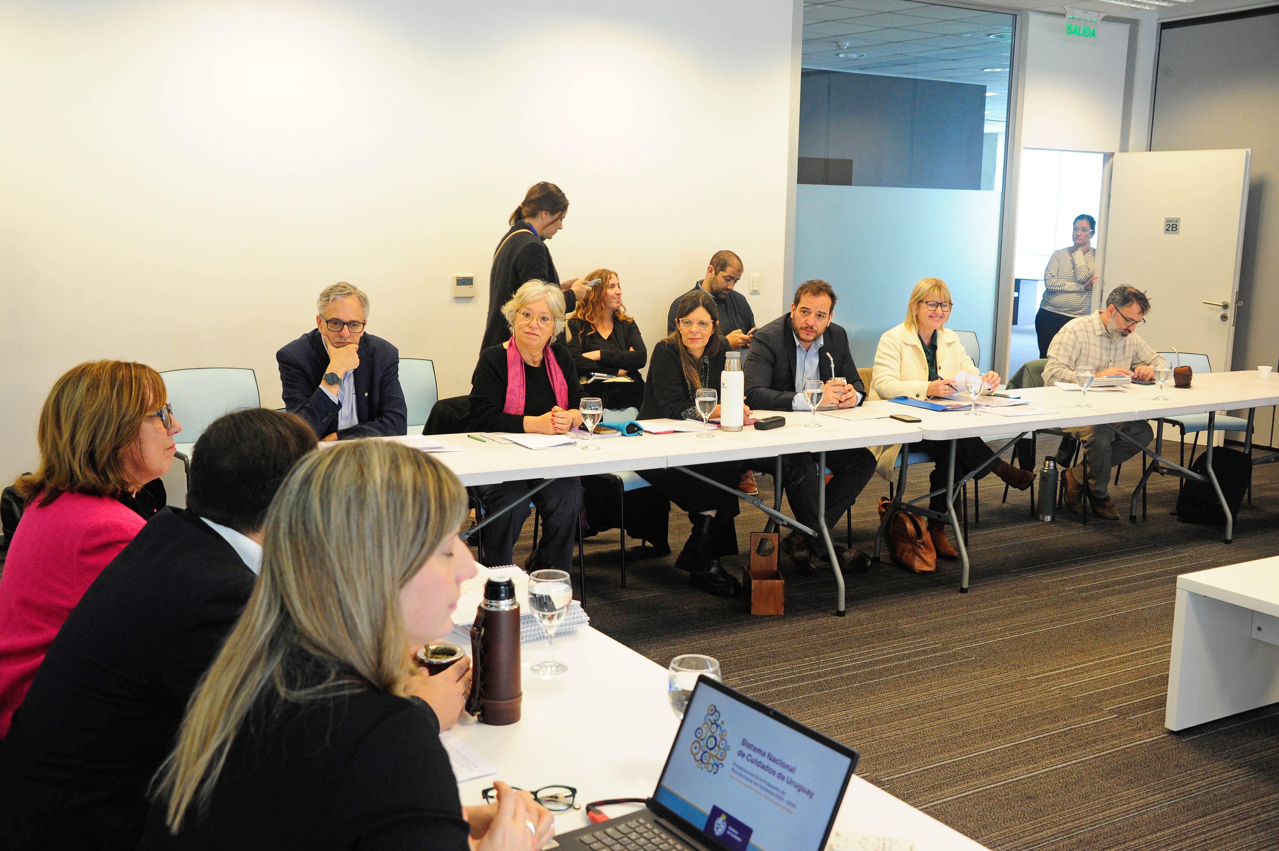 Plano general de la sala de reuniones donde están las autoridades del Consejo Nacional de Cuidados sentadas en mesa en forma de U.