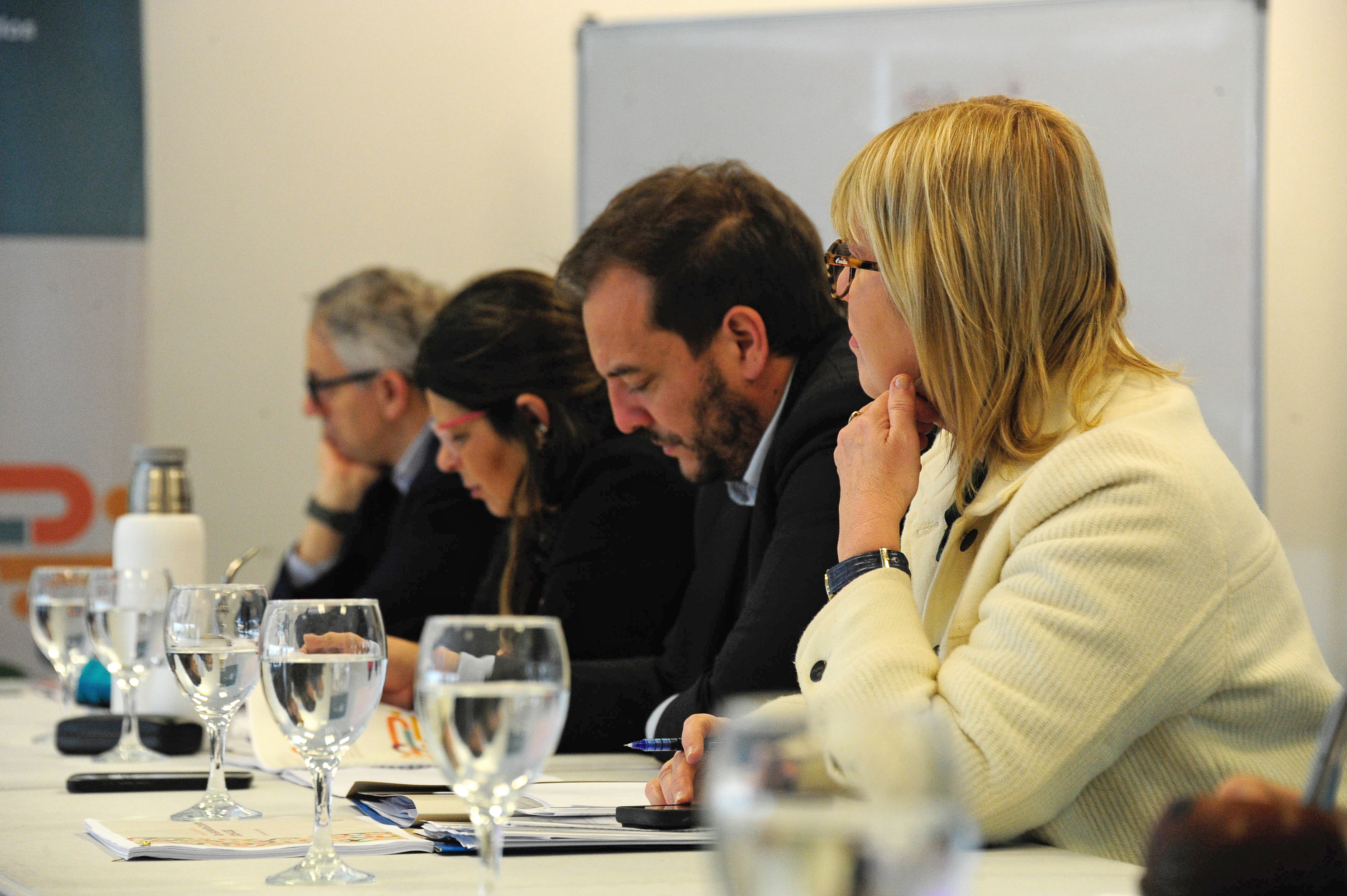 Ministra de Salud Pública, subsecretario de Vivienda, presidenta del INAU y director de OPP sentados en una mesa con vasos de agua en primer plano.