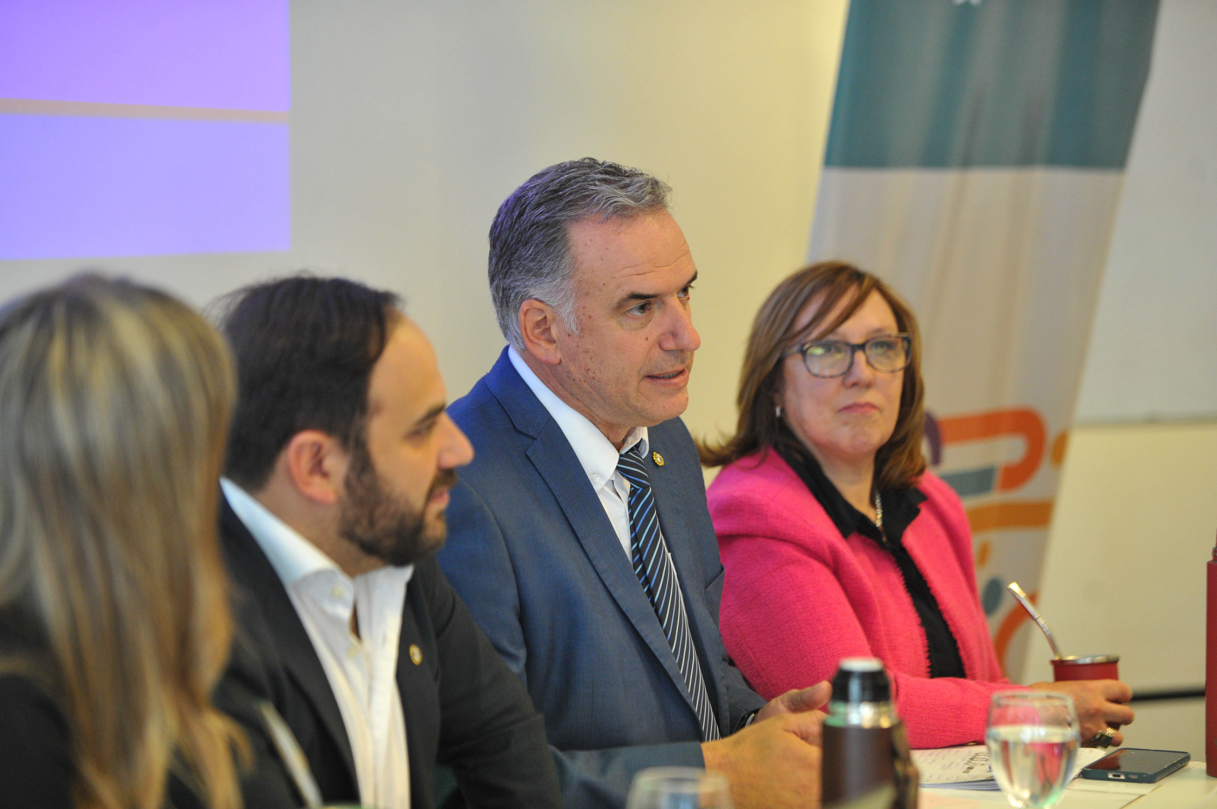 Plano de perfil de Orsi sentado en mesa disertando junto al ministro de Desarrollo Social y autoridades de la cartera.