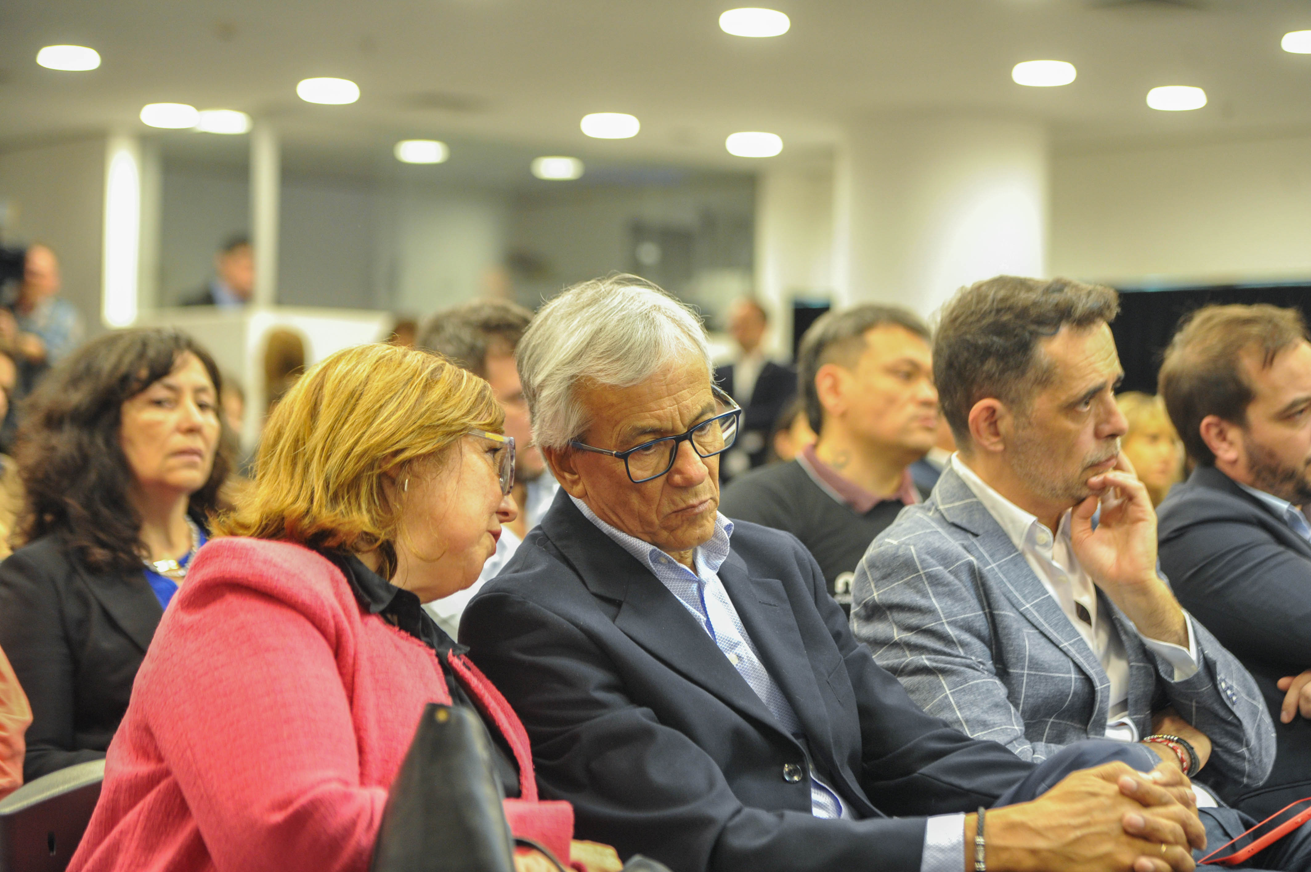 Autoridades de Gobierno sentadas en primera fila de la sala de prensa escuchan atentamente la conferencia.