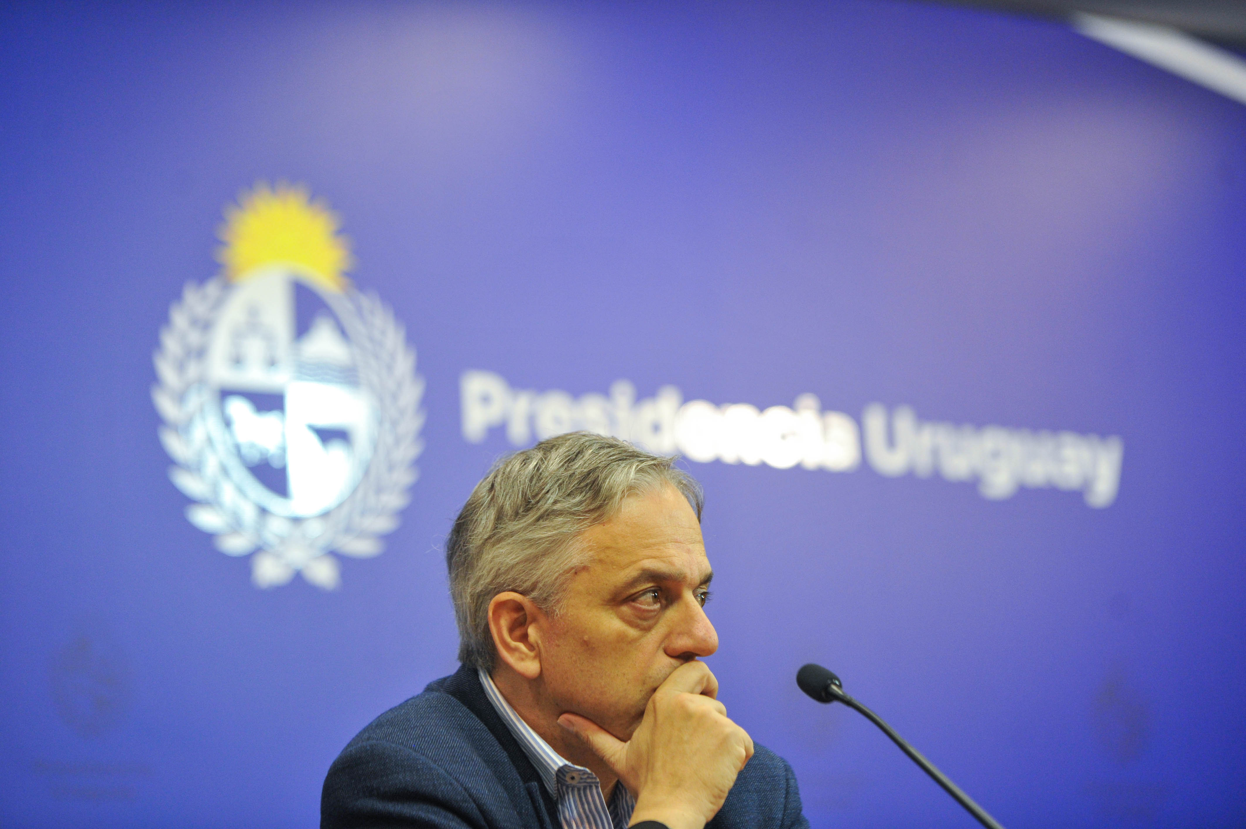 Director de OPP sentado en mesa con micrófono con su mano apoyada en el mentón mira hacia el público.