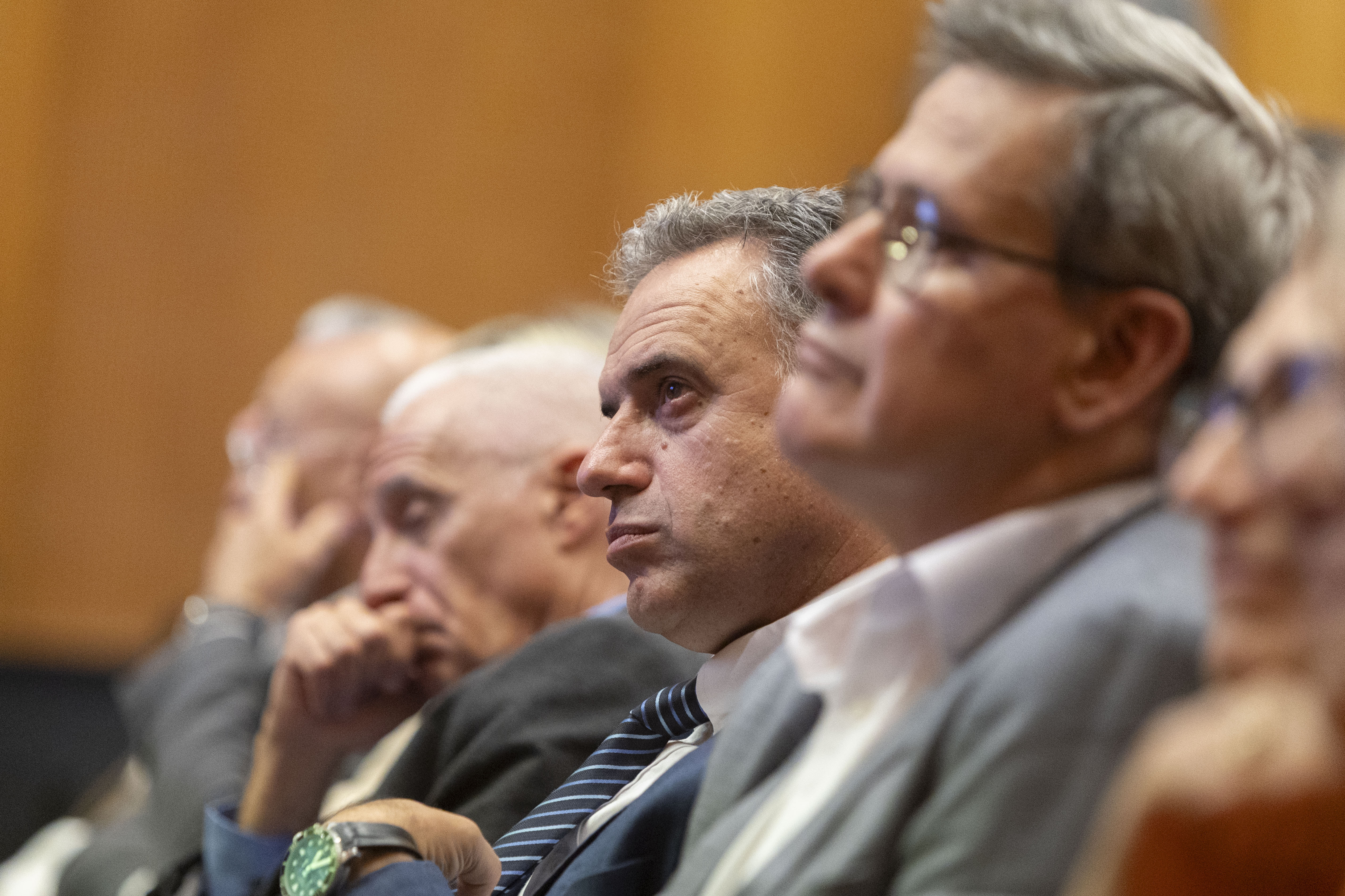 Orsi junto al prosecretario de Presidencia y otros asistentes escucha atentamente una disertación, sentado en el auditorio.