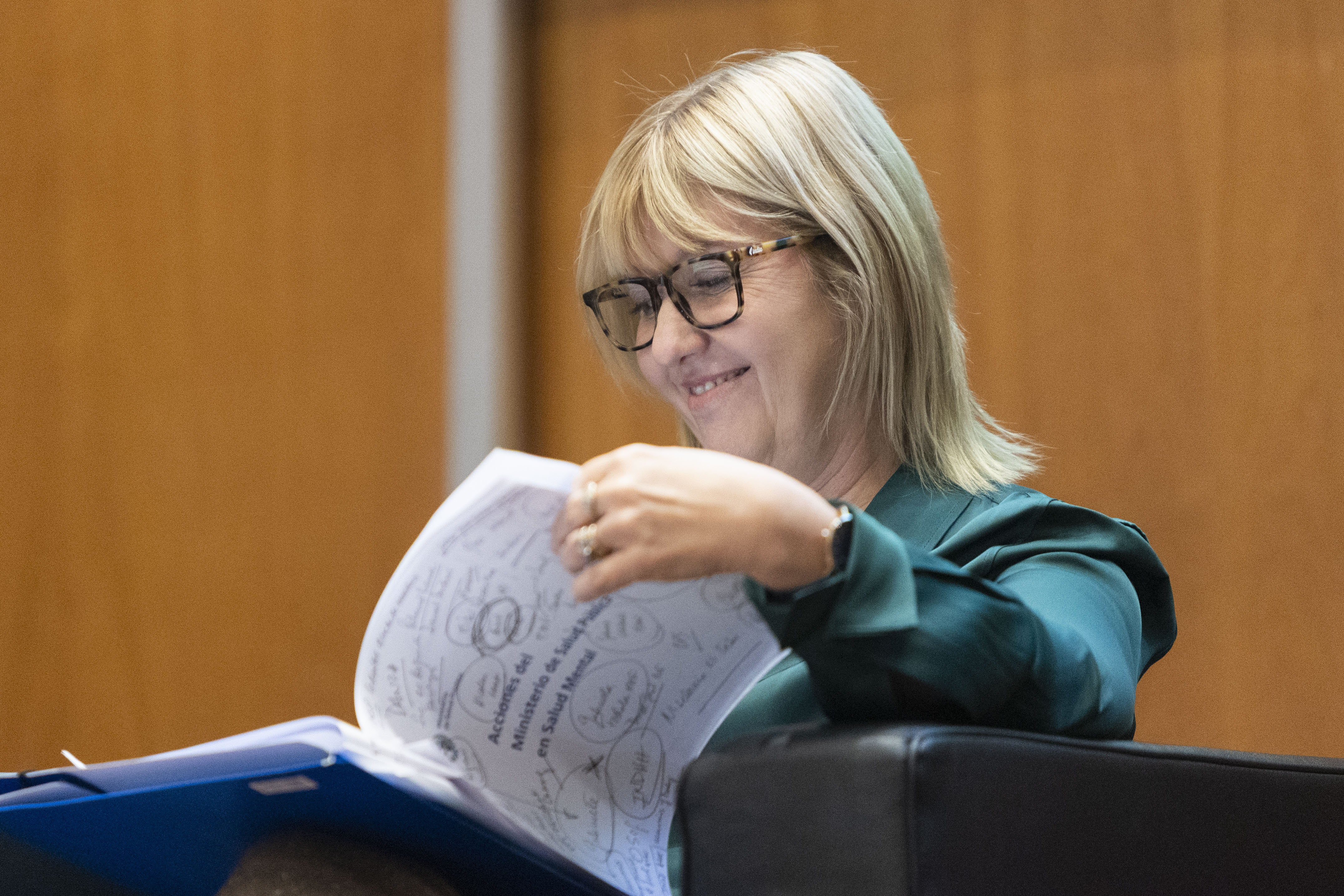La ministra de Salud Pública revisa un informe en el escenario mientras espera para disertar.
