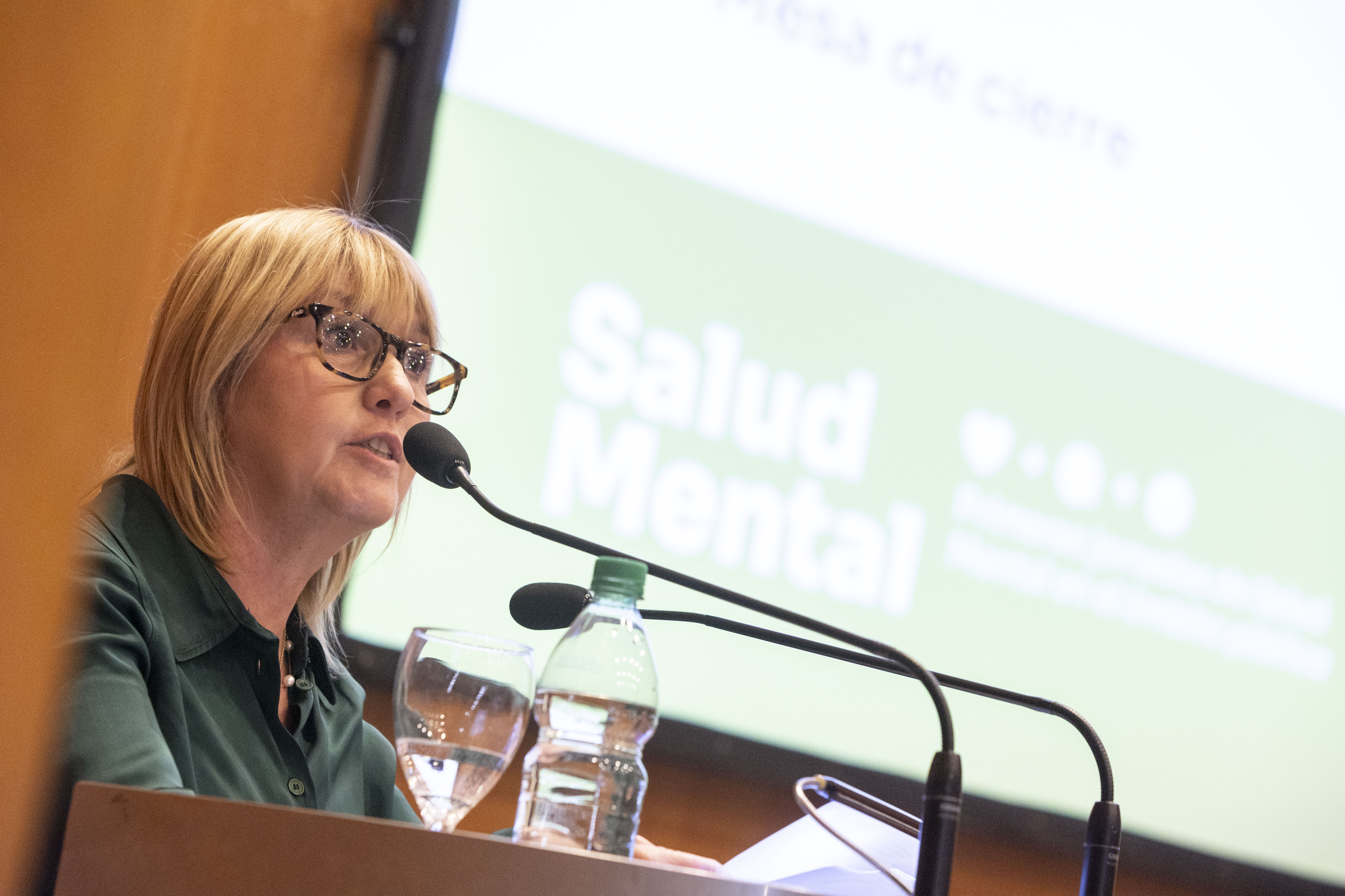 Ministra de Salud Pública diserta de pie en atril con micrófono. Atrás se observa una gran pantalla con la inscripción: Salud Mental.