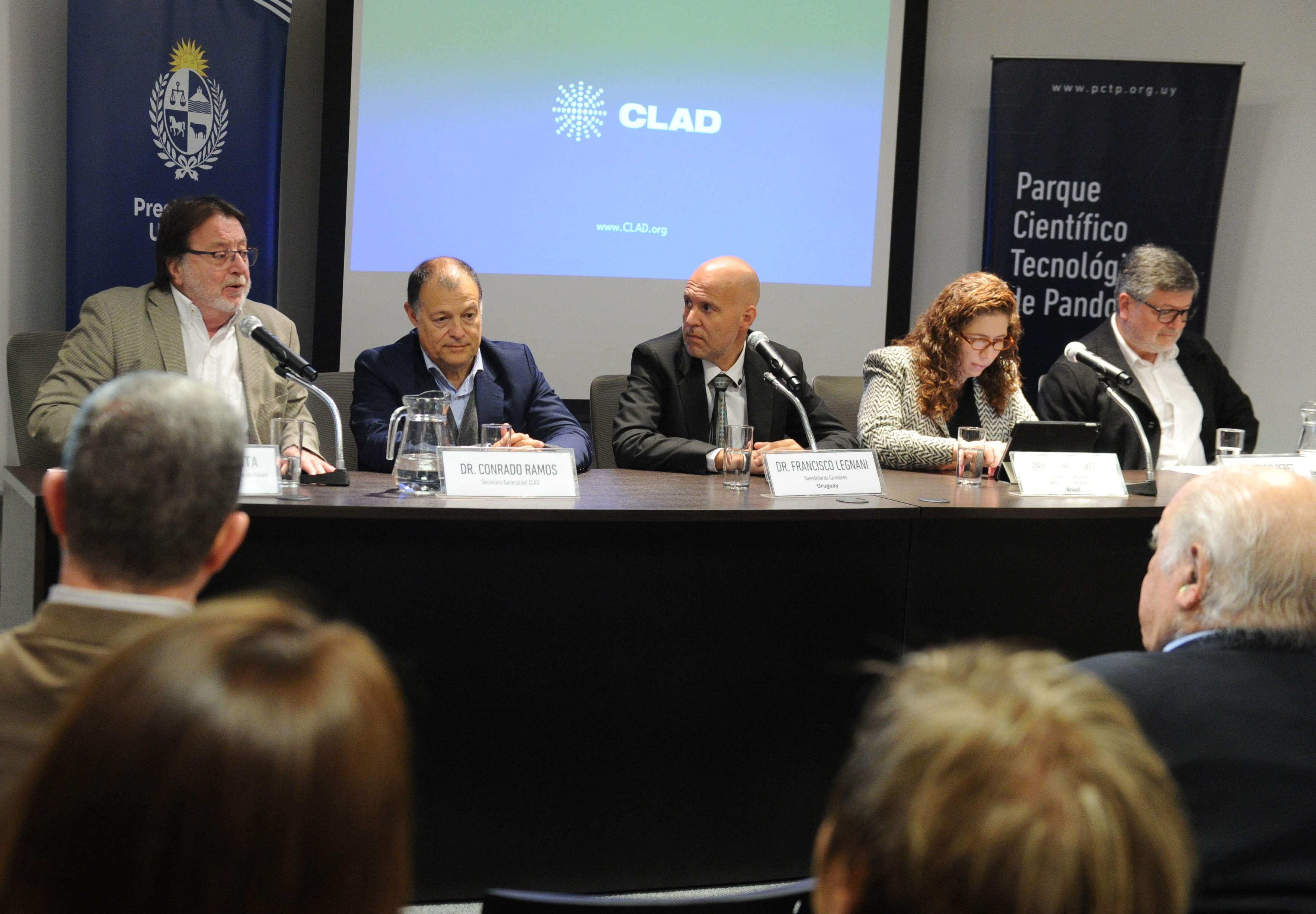 Autoridades de ambas instituciones sentadas en mesa con micrófonos esperan para disertar.