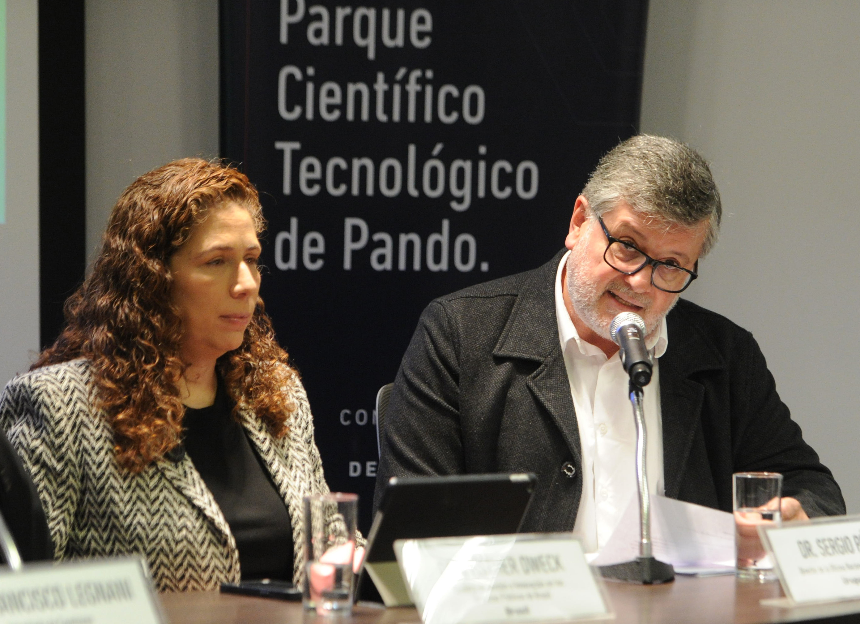 El Director de la Oficina de Servicio Civil expone en la mesa principal, mientras la ministra de Brasil a su lado lo observa.