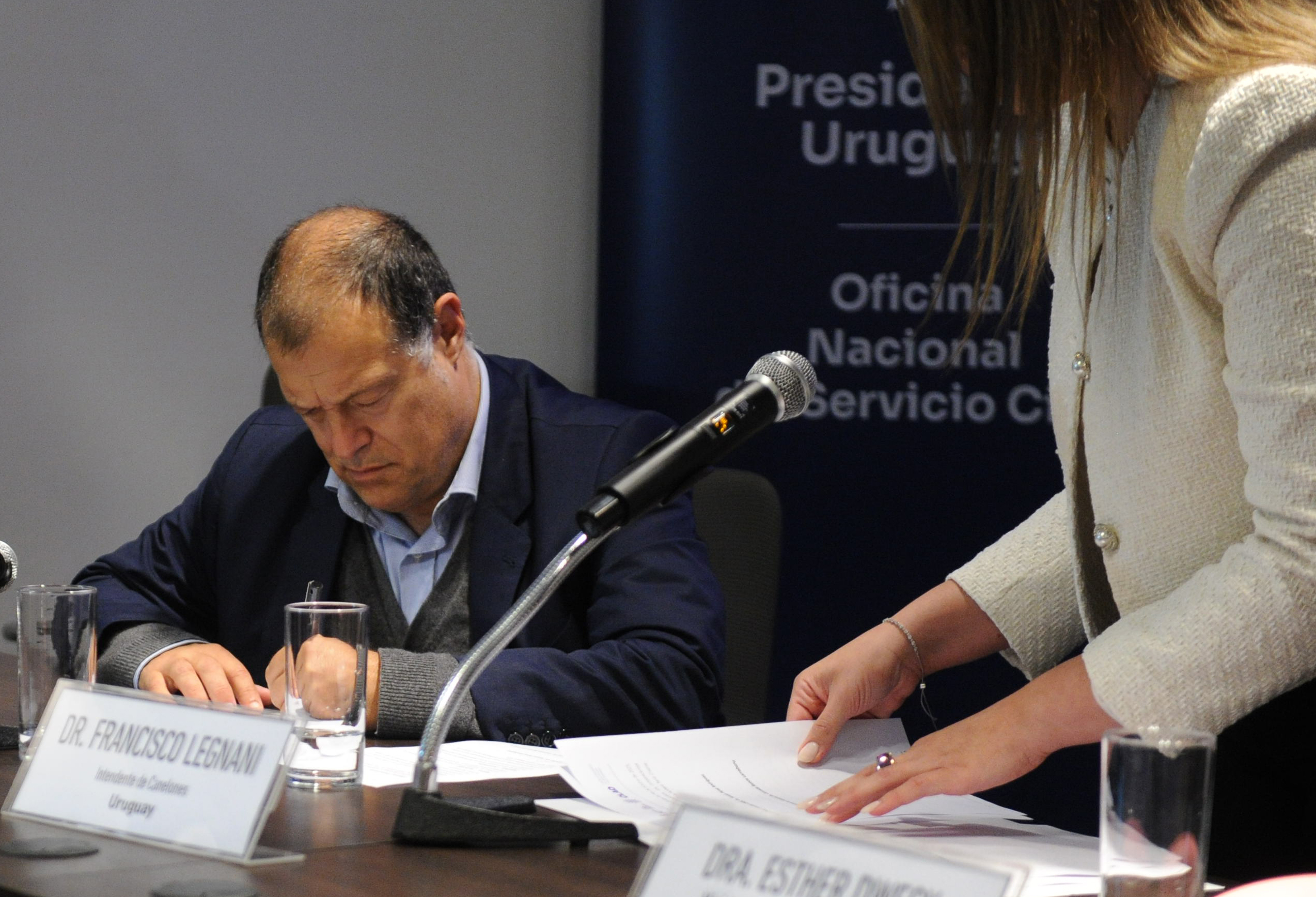 Secretario general del Centro Latinoamericano de Administración para el Desarrollo firma un documento sentado en la mesa principal.